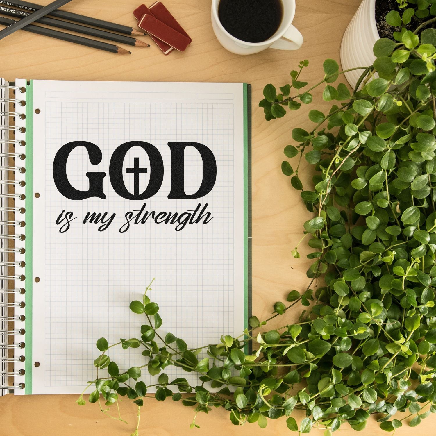 Christian rubber stamp design reading God is my strength in a planner on a desk with coffee, pencils, and greenery.