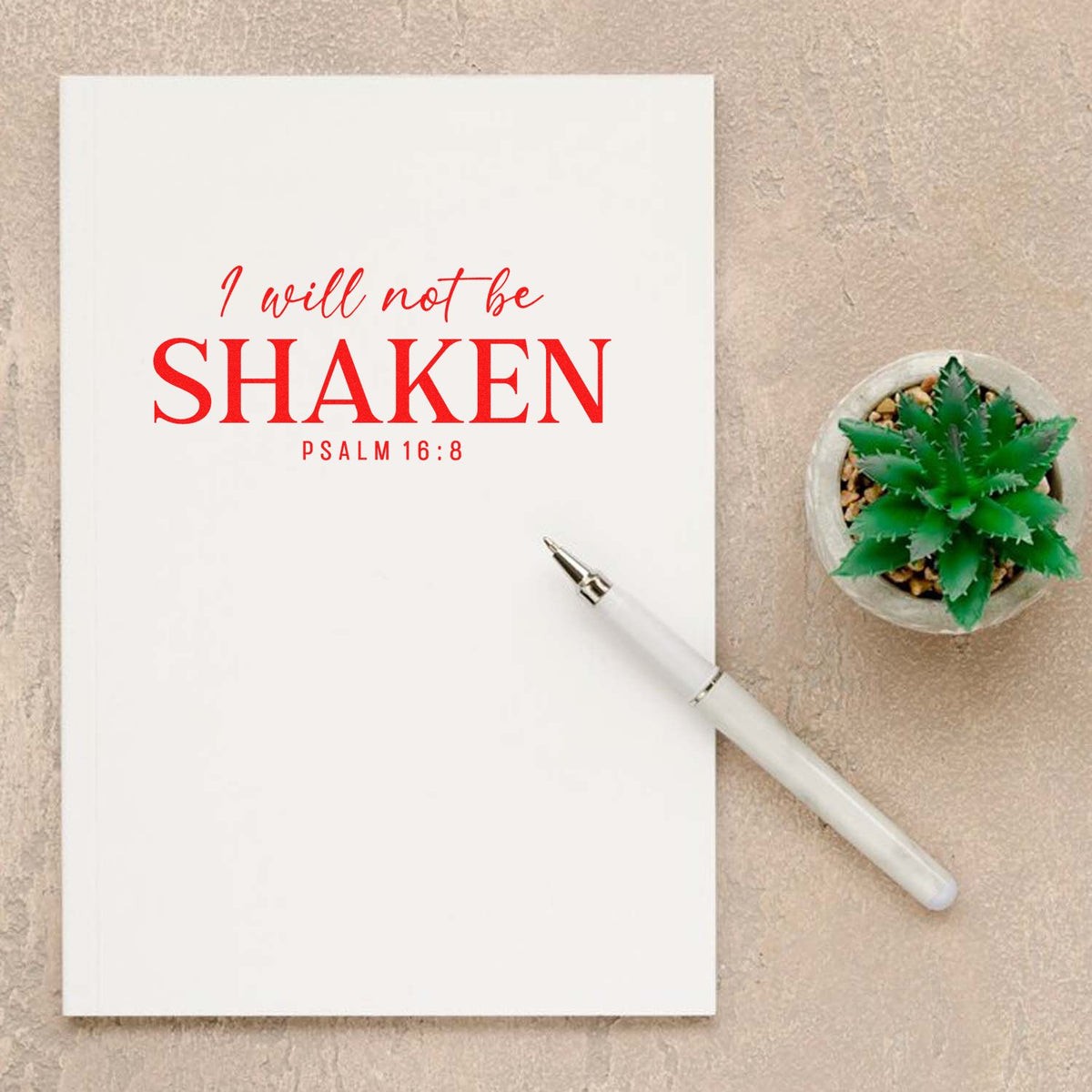Bible verse rubber stamp design reading I will not be shaken Psalm 16:8 on notebook with pen and succulent.