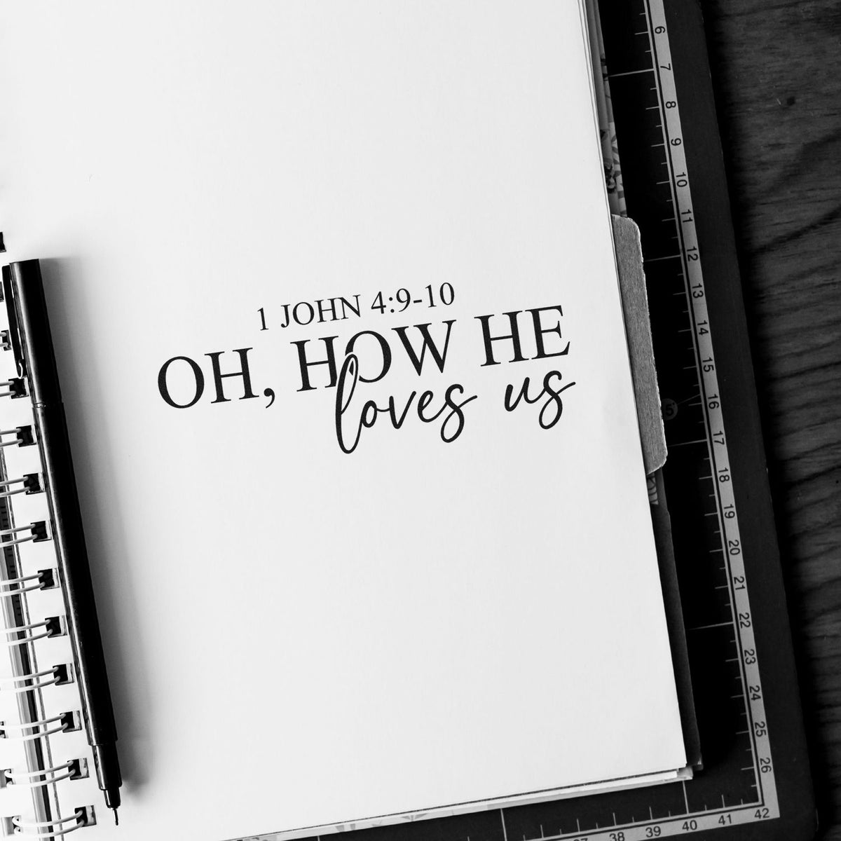 Bible verse rubber stamp on notebook page reading 1 John 4:9-10 Oh, how He loves us for Christian journaling.