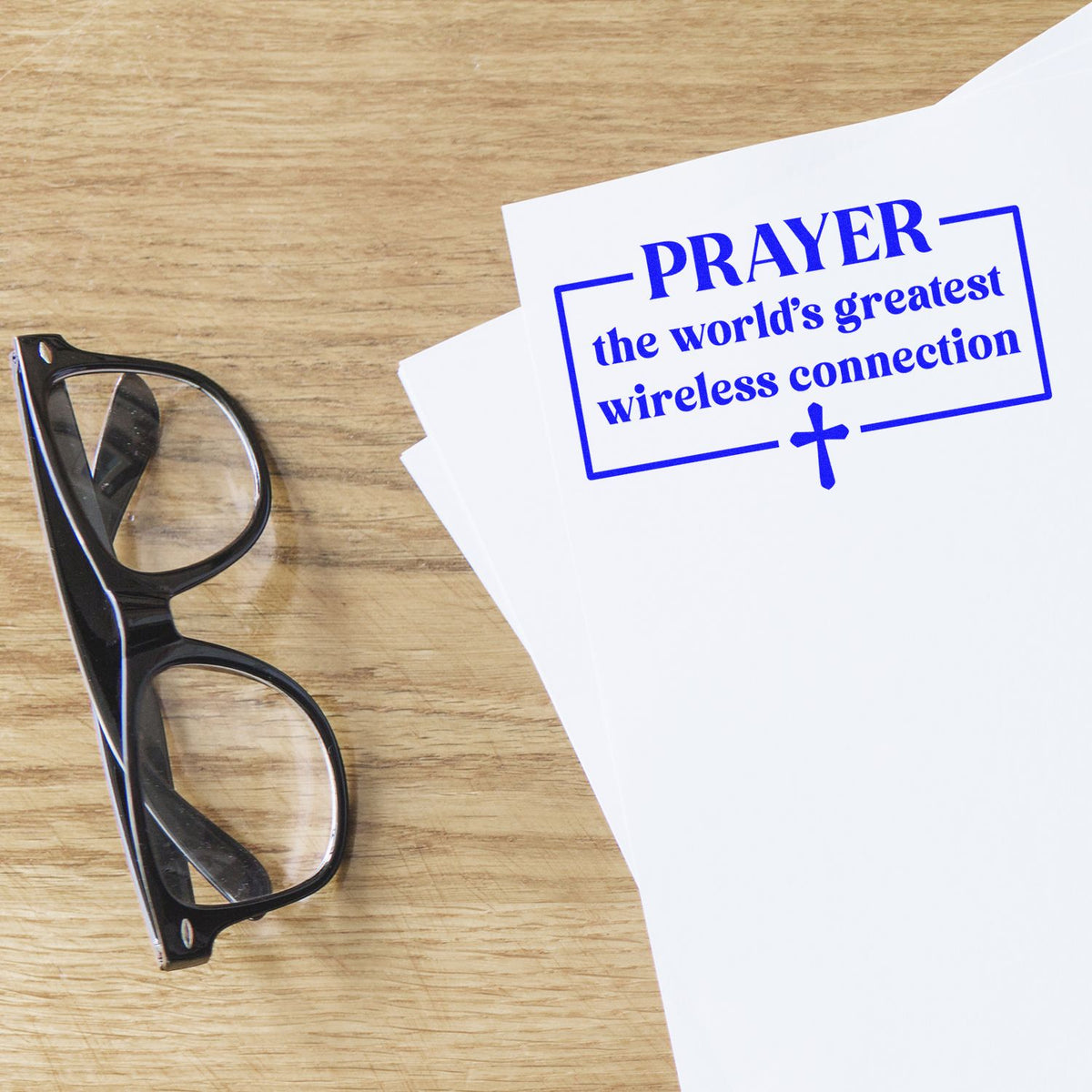 Prayer rubber stamp on paper beside eyeglasses, reading the worlds greatest wireless connection with a cross.