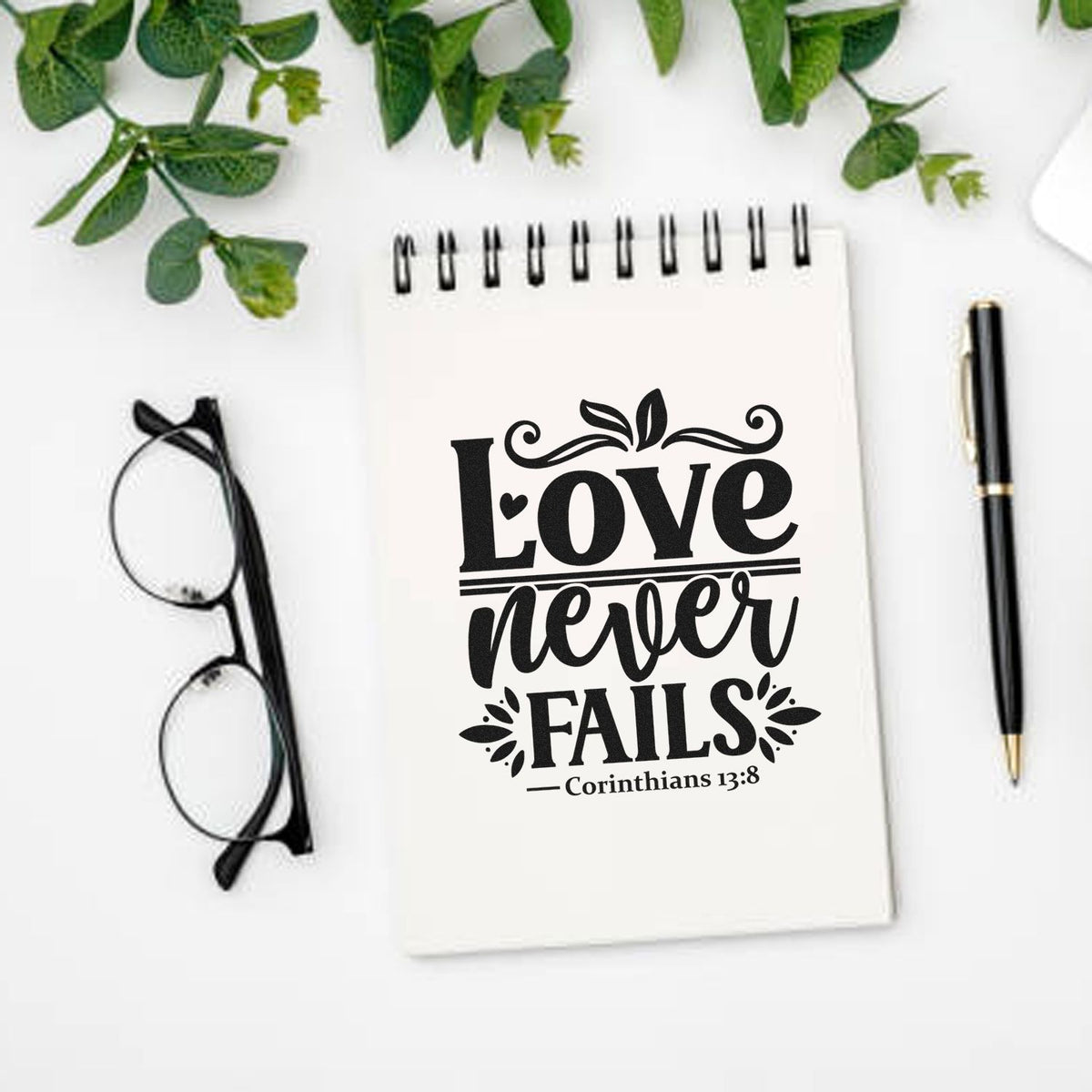 Love Never Fails Corinthians 13:8 rubber stamp design on a notebook, ideal for faith-based Bible journaling and crafts.