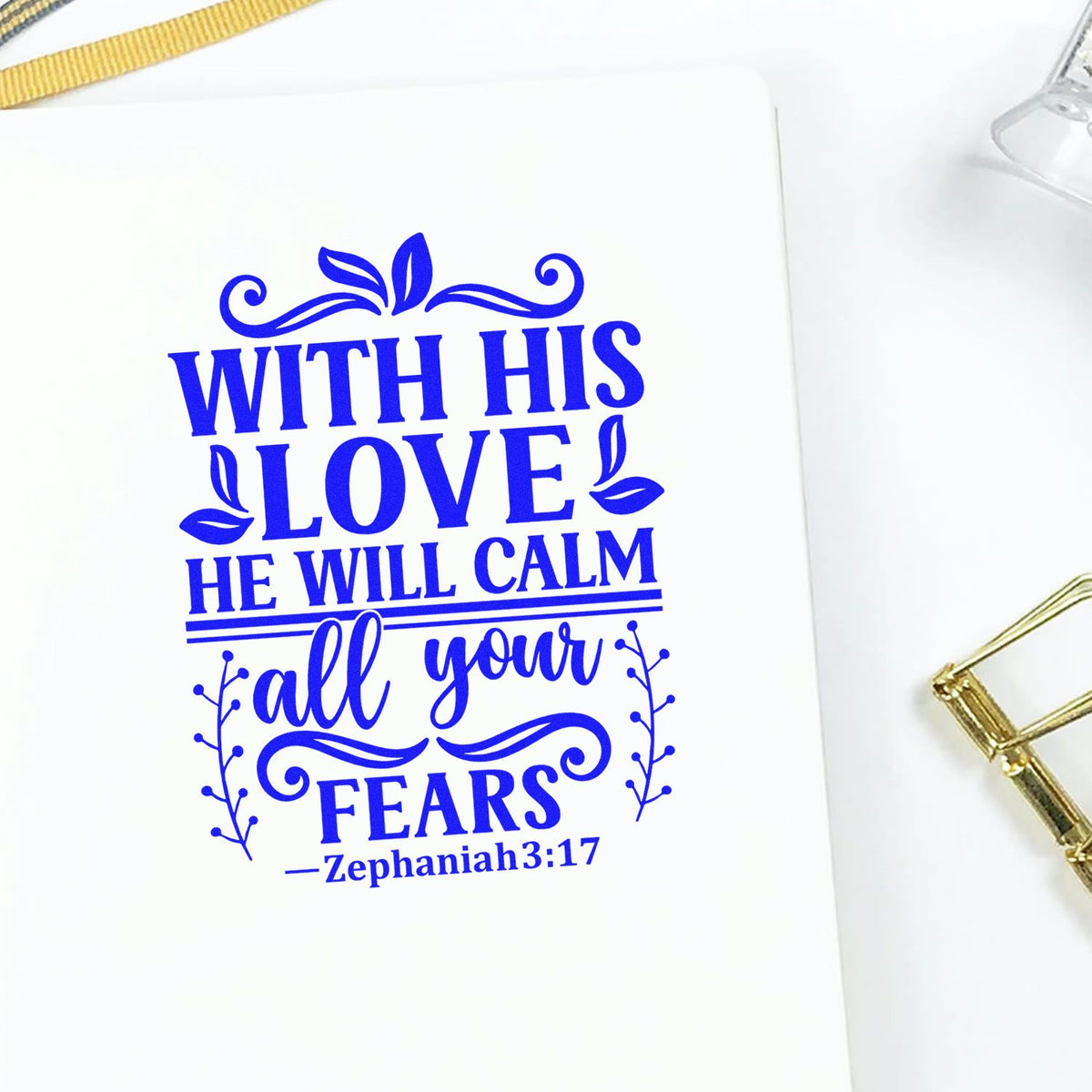 Blue Christian rubber stamp design with Zephaniah 3:17 quote, With His love He will calm all your fears, on white paper.
