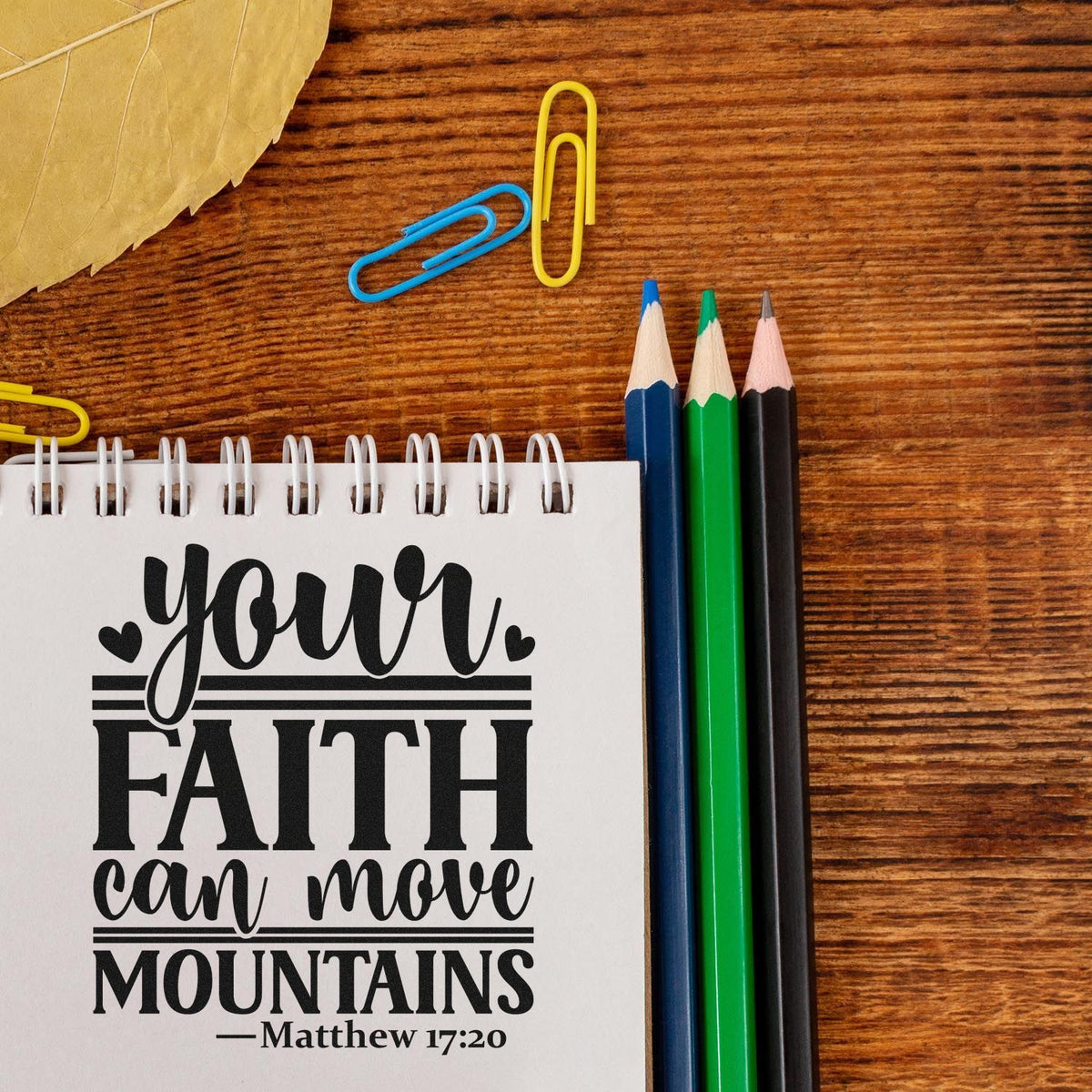 Christian rubber stamp design with Matthew 17:20 quote, Your faith can move mountains, on a notebook with pencils.