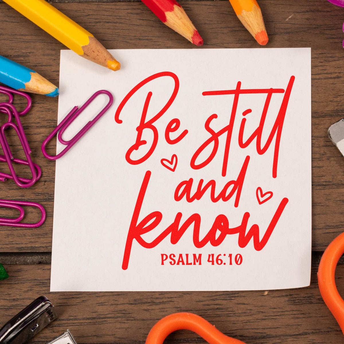Bible verse rubber stamp design reading Be still and know Psalm 46:10 in red script on a white note with school supplies.