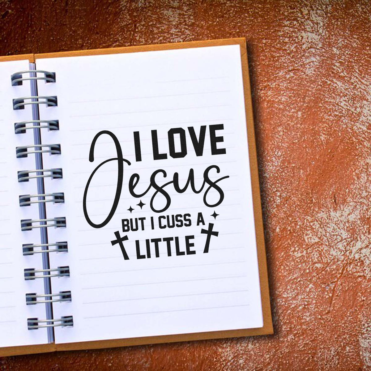 Christian novelty rubber stamp design reading I Love Jesus But I Cuss a Little on a spiral notebook page.