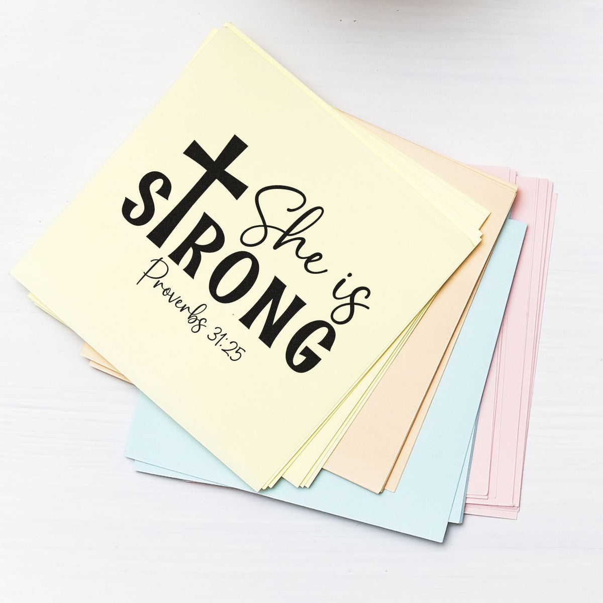 Custom Christian rubber stamp design reading She is Strong with Proverbs 31:25 on pastel paper cards.