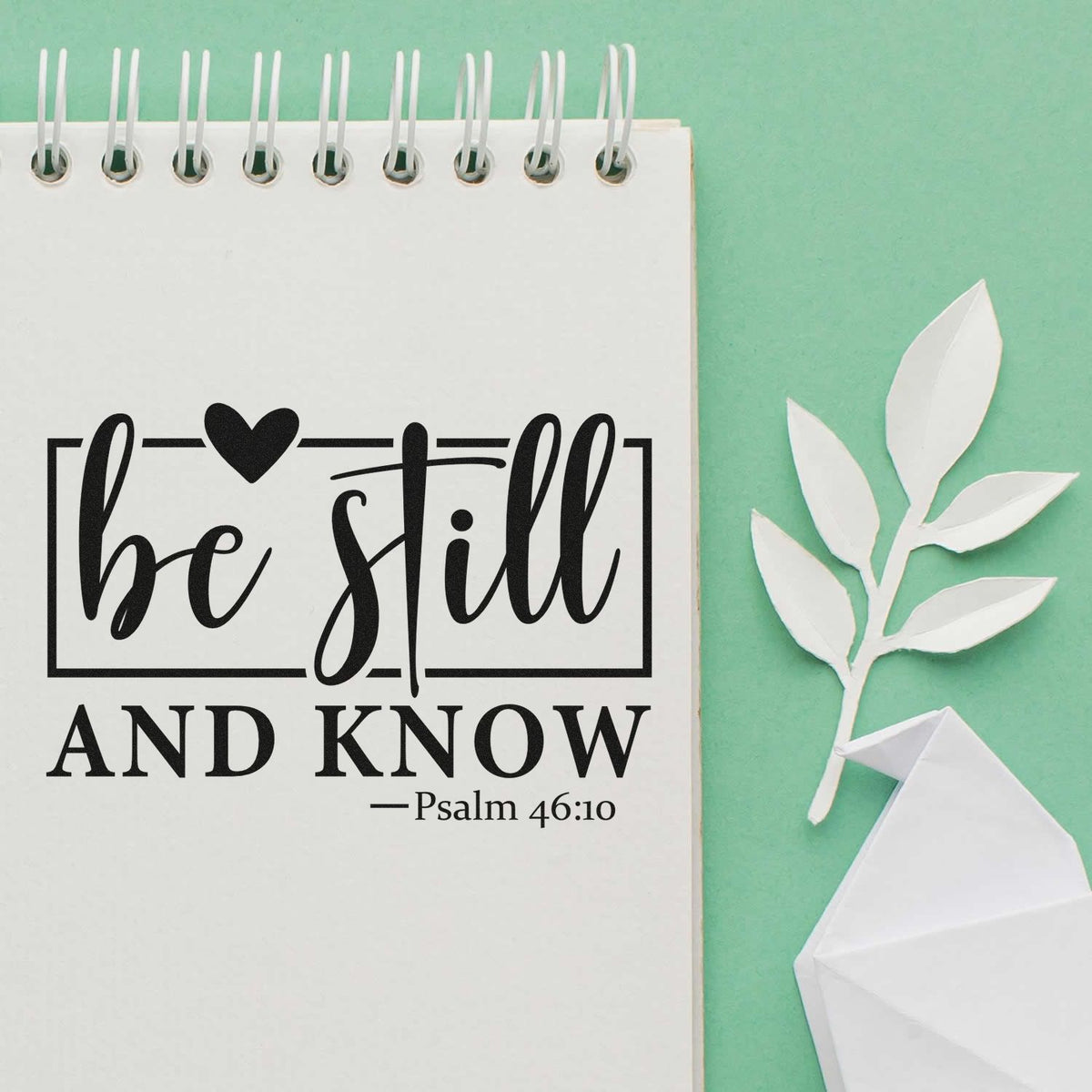 Bible verse rubber stamp impression reading Be Still and Know with Psalm 46:10 on a notebook page.