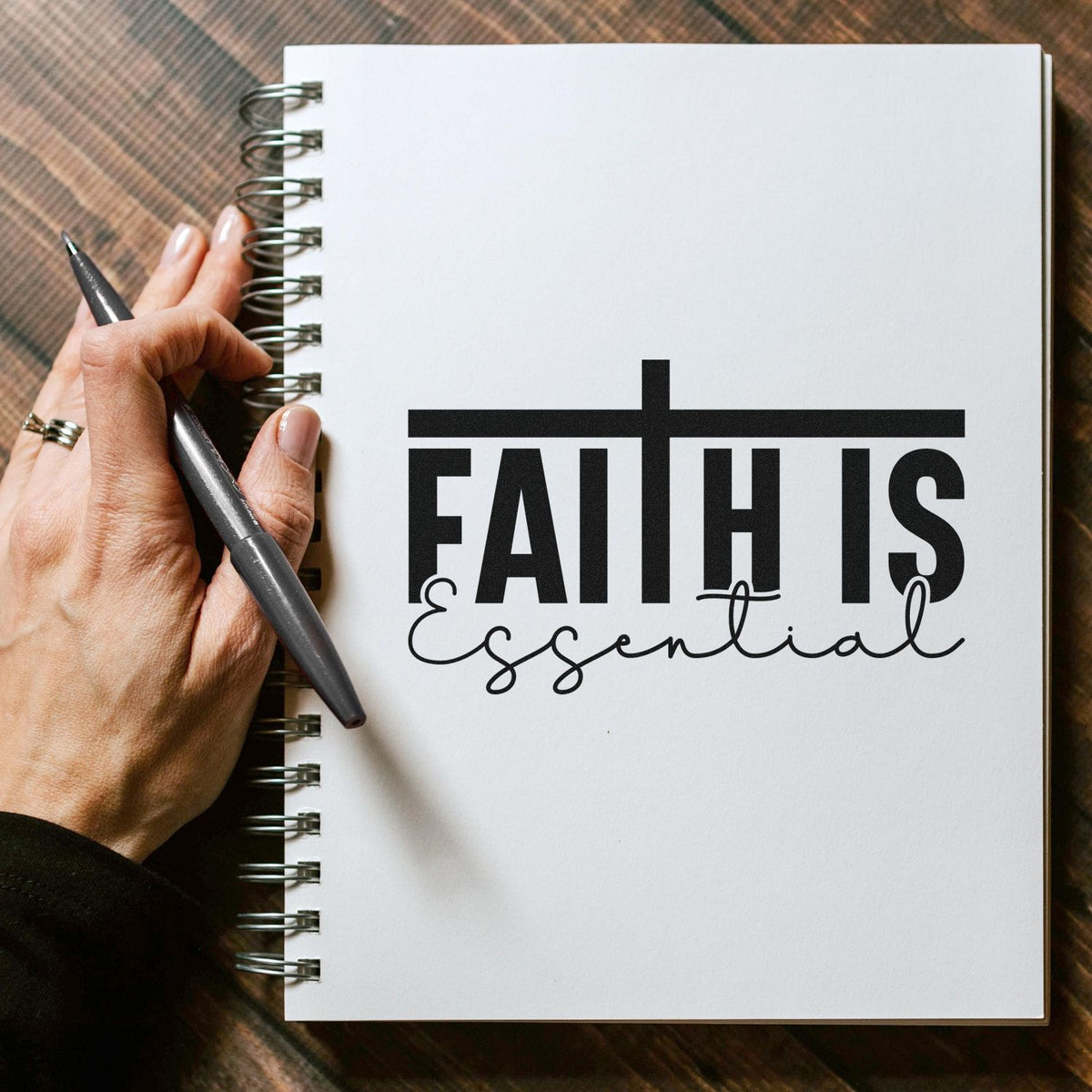 Essential Faith Crossbar Lettering Slim Pre-Inked Stamp imprint stamped in black ink. Bold "Faith is" lettering sits beneath a crossbar, with "Essential" in flowing script below.