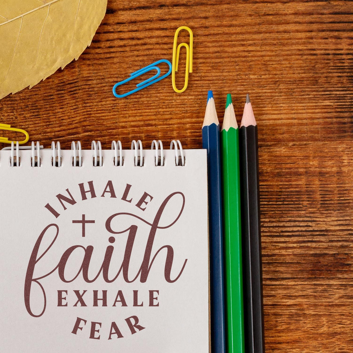 Inspirational rubber stamp design with Inhale Faith, Exhale Fear on a notebook beside pencils and paper clips.