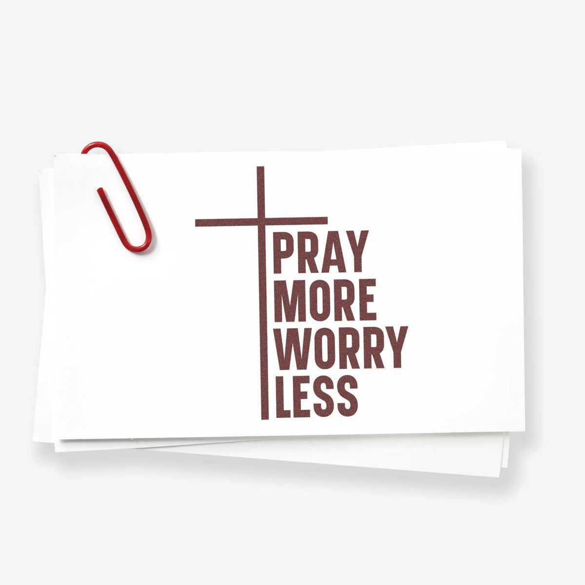 Christian rubber stamp design with cross and Pray More Worry Less on stacked paper cards with red paperclip.