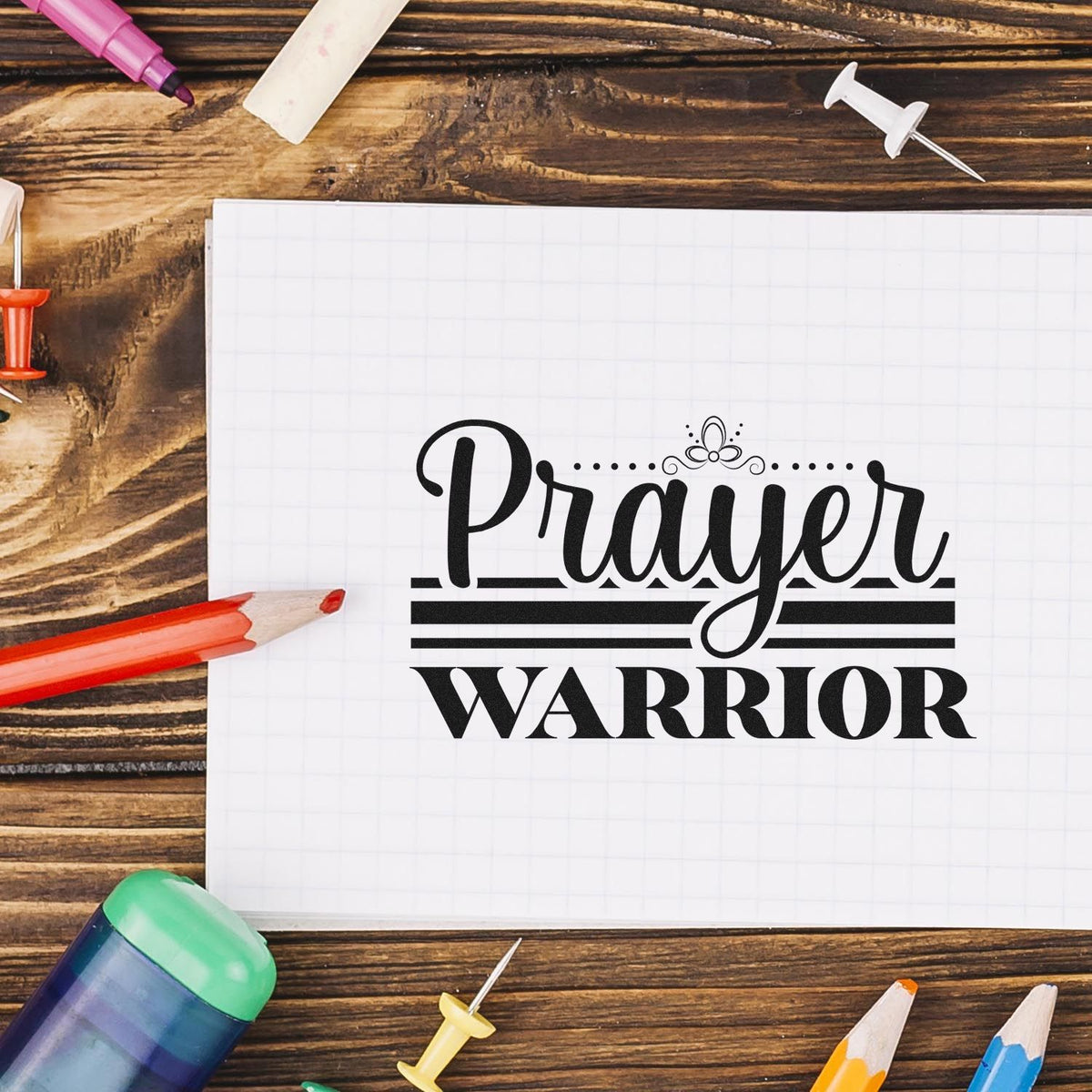 Prayer Warrior rubber stamp design on notebook paper, surrounded by art supplies on a rustic wood desk.