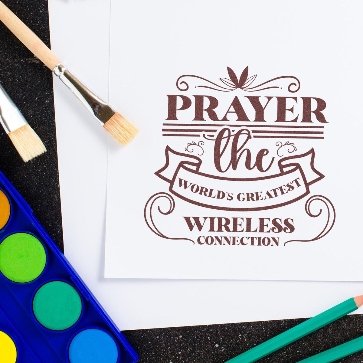 Prayer rubber stamp design on paper with paintbrushes and watercolor palette, featuring worlds greatest wireless connection text.