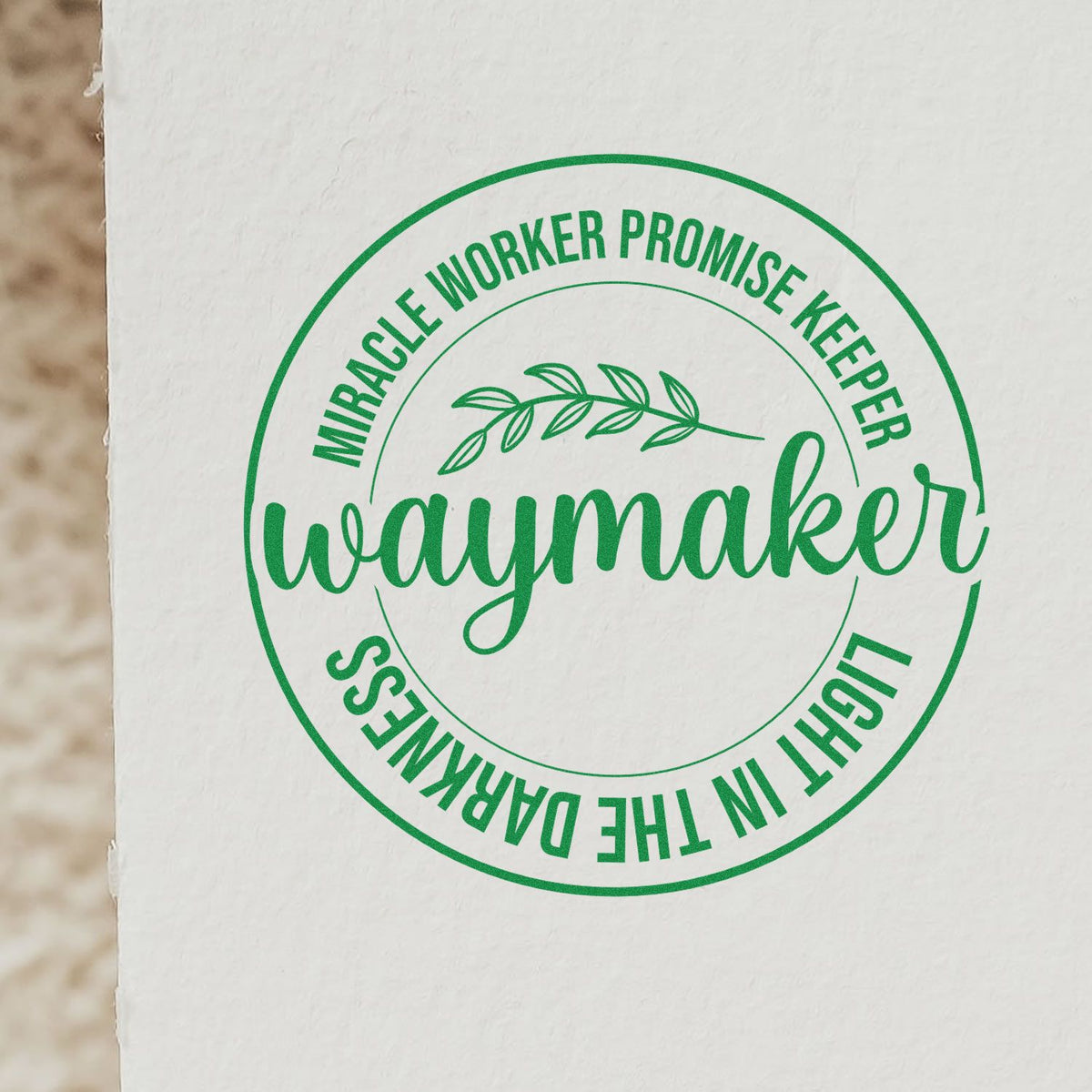 Green Waymaker rubber stamp design with circular Christian text: Miracle Worker, Promise Keeper, Light in the Darkness on white paper.