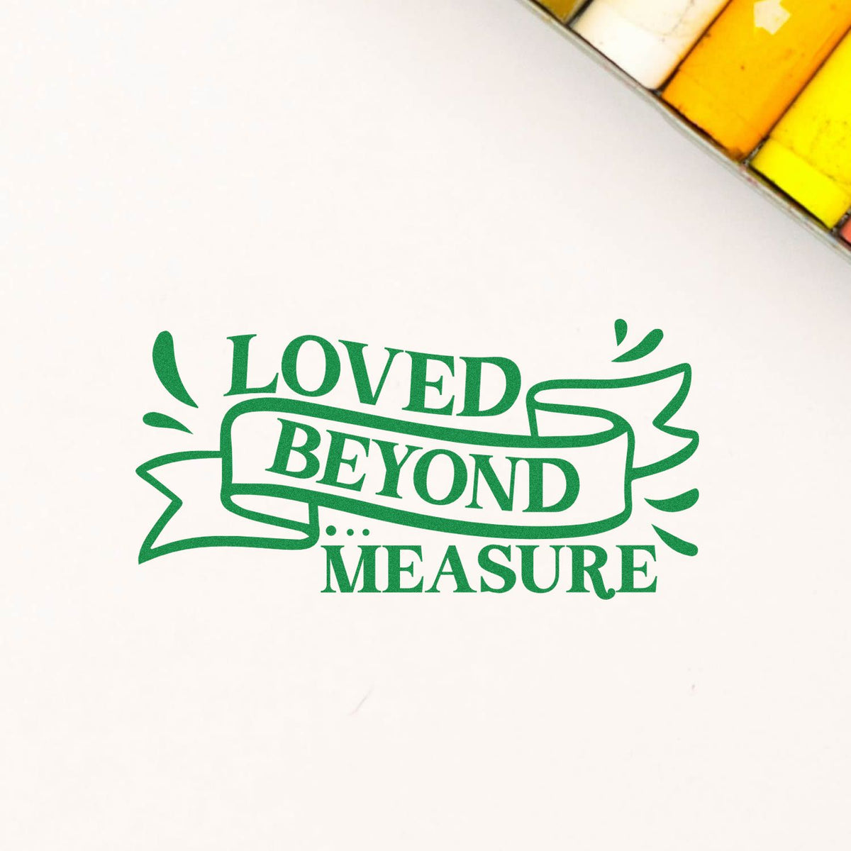 Green rubber stamp design reading Loved Beyond Measure with decorative banner on white paper.