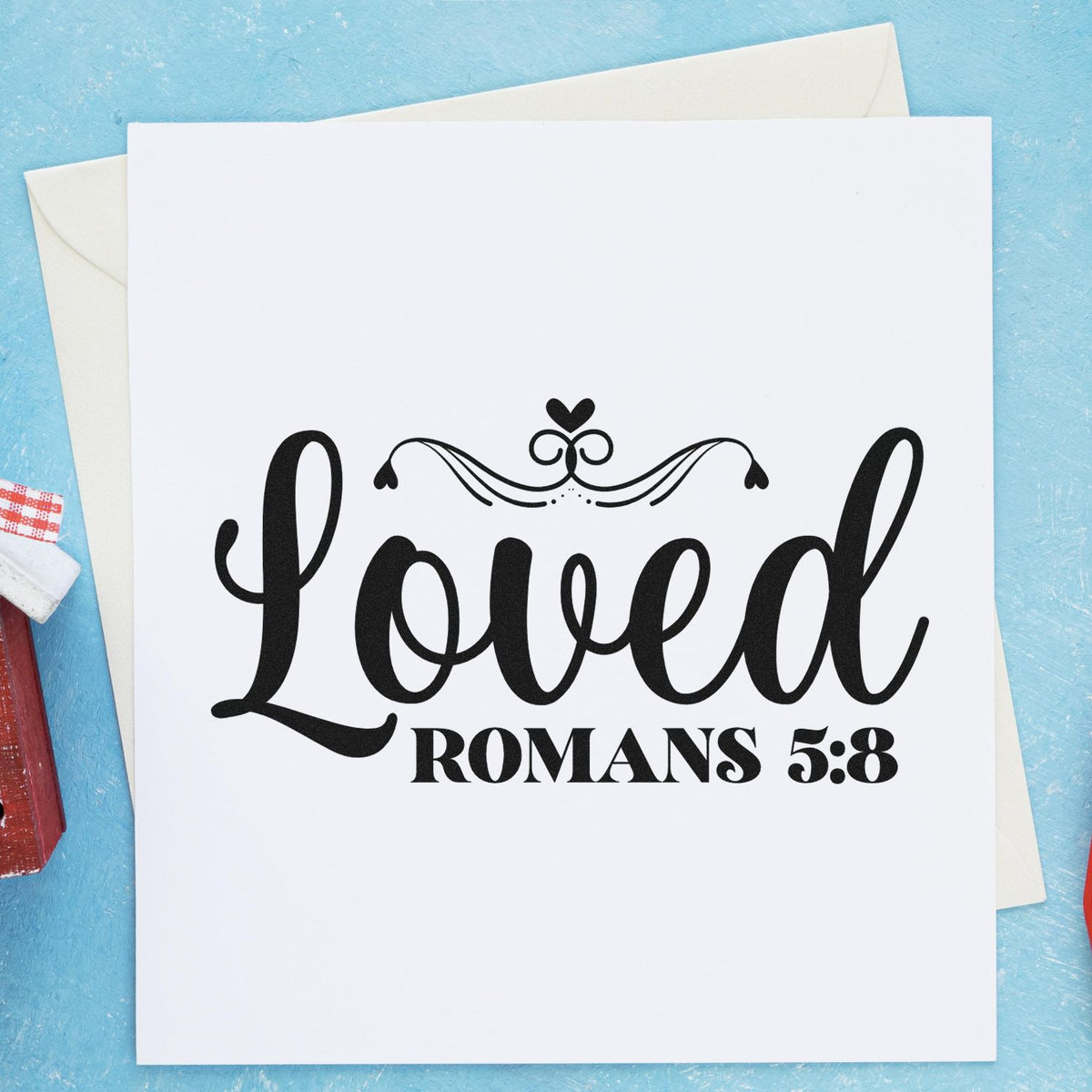 Christian rubber stamp design featuring Loved and Romans 5:8 with decorative heart flourish on a white card.
