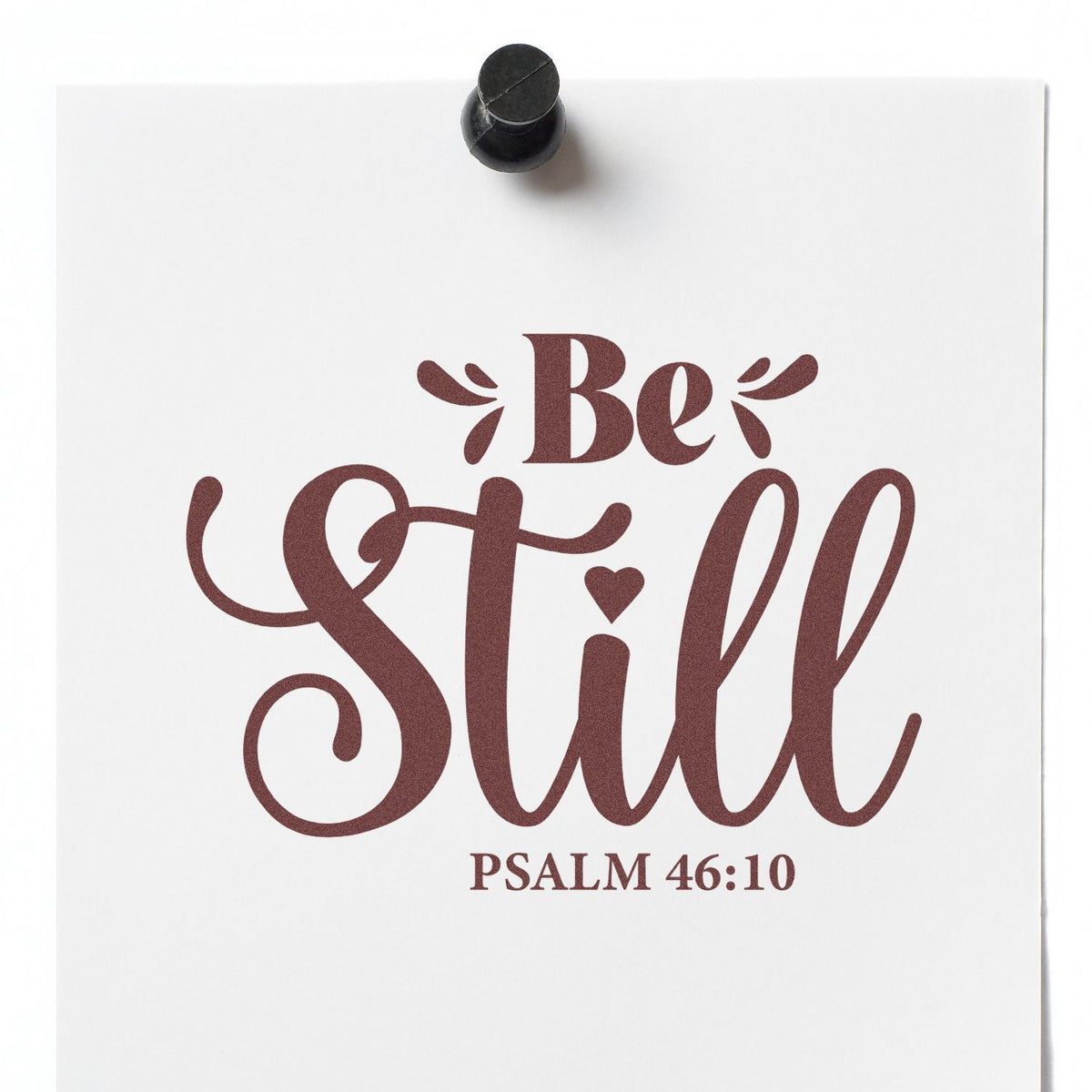 Bible verse rubber stamp design reading Be Still with Psalm 46:10 printed in decorative lettering on white paper.