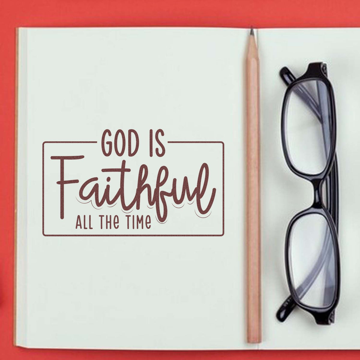 Christian rubber stamp reading God Is Faithful All the Time on a notebook page with pencil and glasses.
