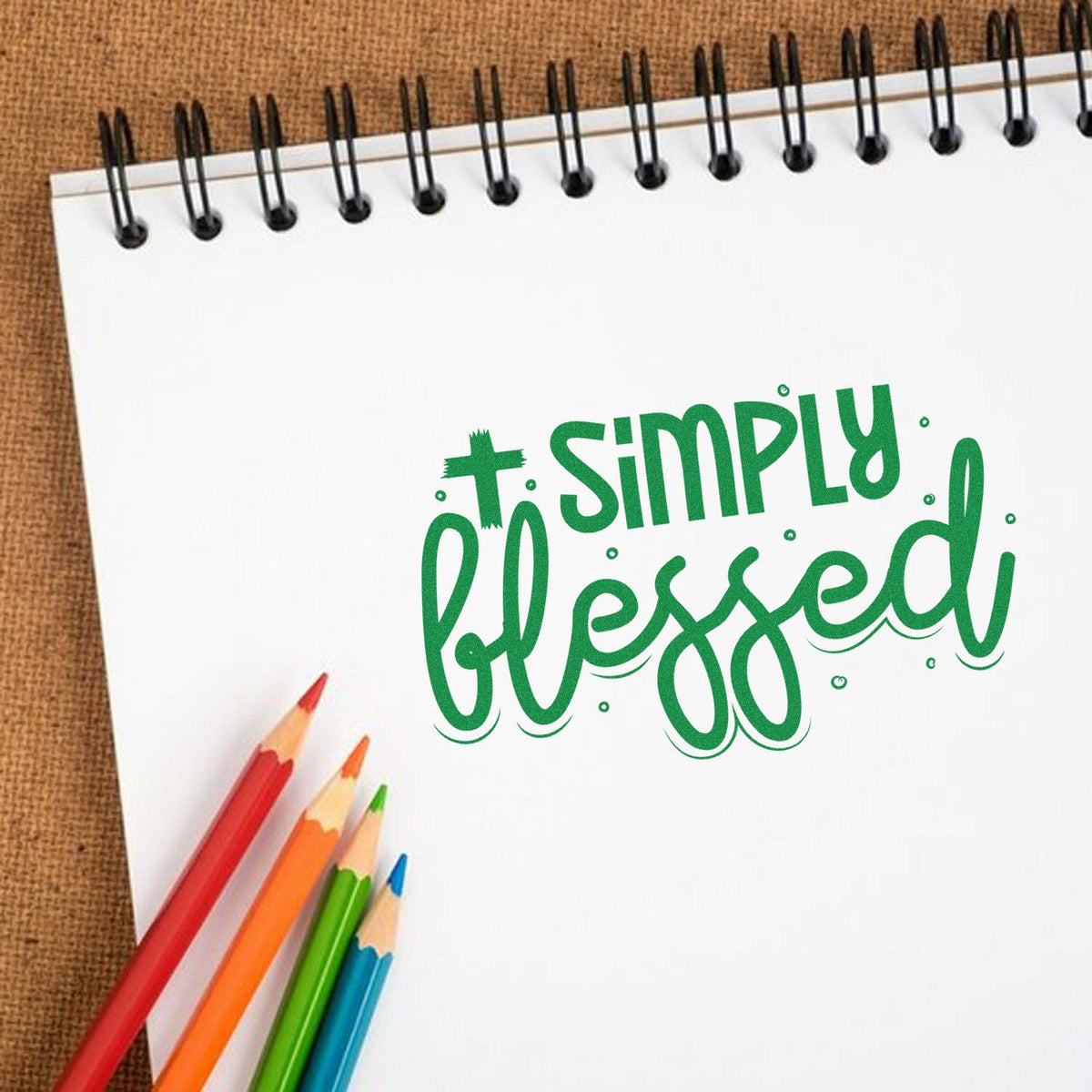 Simply blessed rubber stamp design on spiral notebook with colored pencils, ideal for faith-based crafts and journaling.