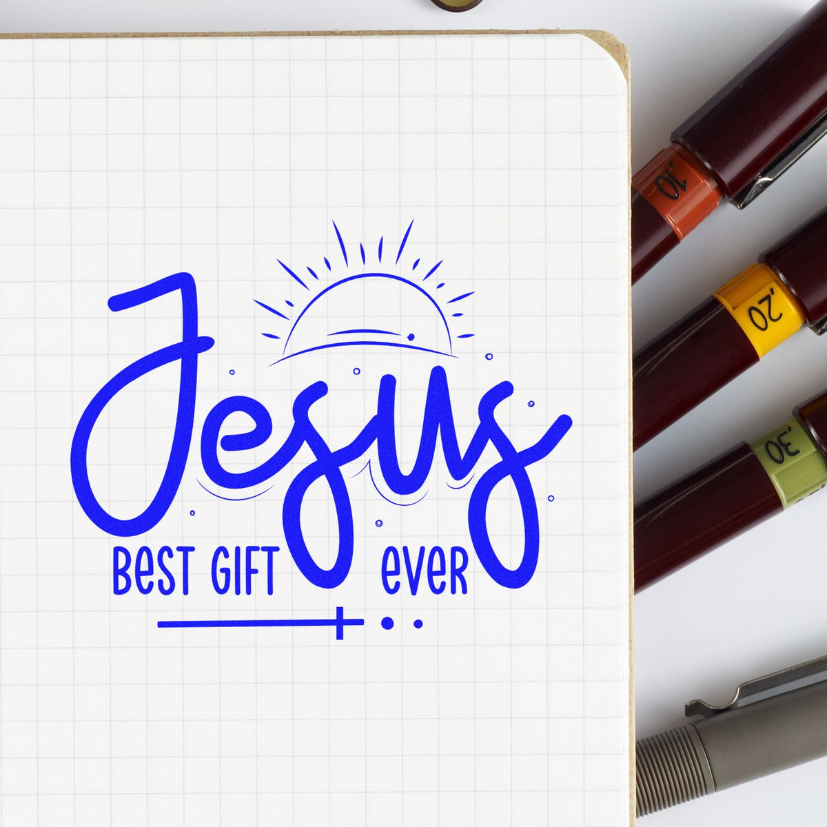 Christian rubber stamp reading Jesus Best Gift Ever in blue on notebook paper.