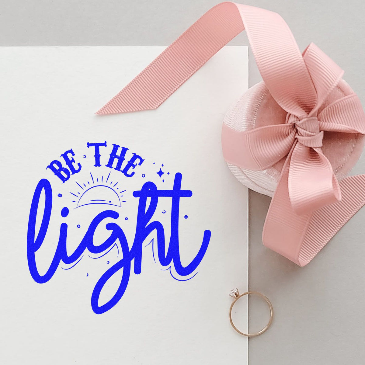 Custom rubber stamp with Be the Light quote for gift packaging, shown on a card with pink ribbon.
