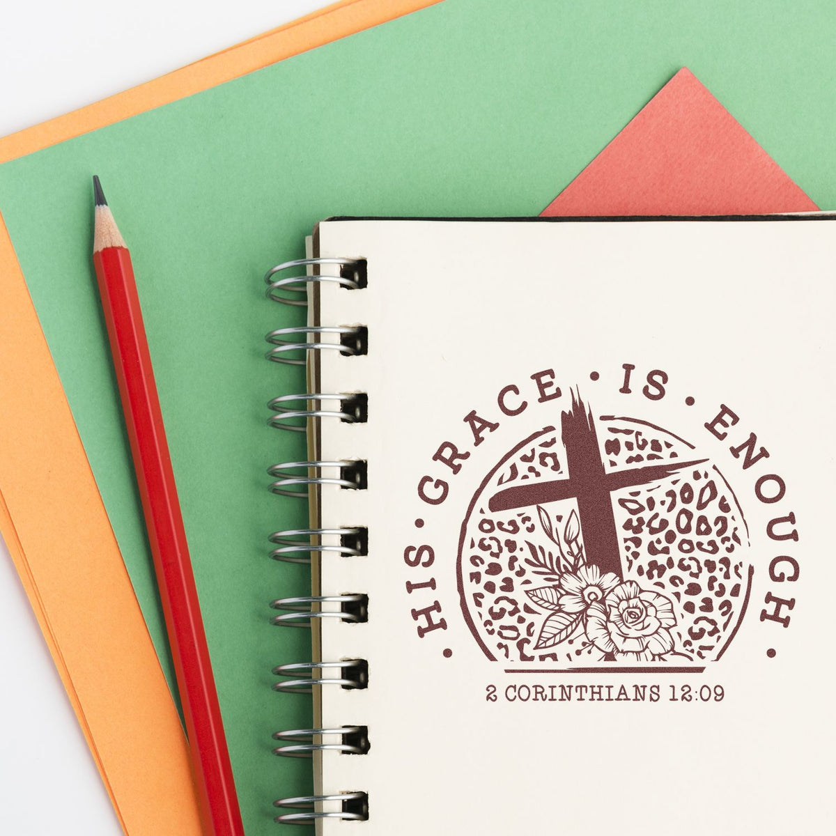 Christian rubber stamp design reading His grace is enough with cross, flowers, and 2 Corinthians 12:9 on notebook.