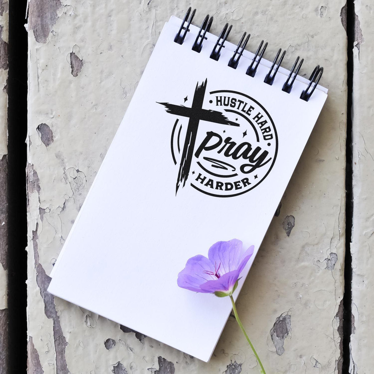Custom rubber stamp design with Hustle Hard Pray Harder slogan and cross logo on a spiral notebook.
