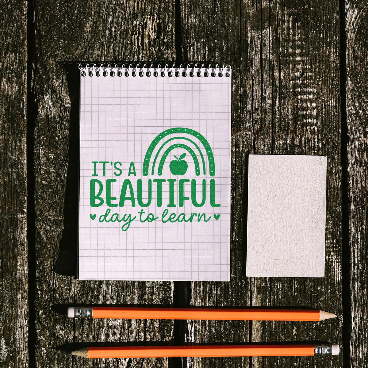 Back-to-school rubber stamp design reading Its a beautiful day to learn with apple and rainbow on a notebook page.