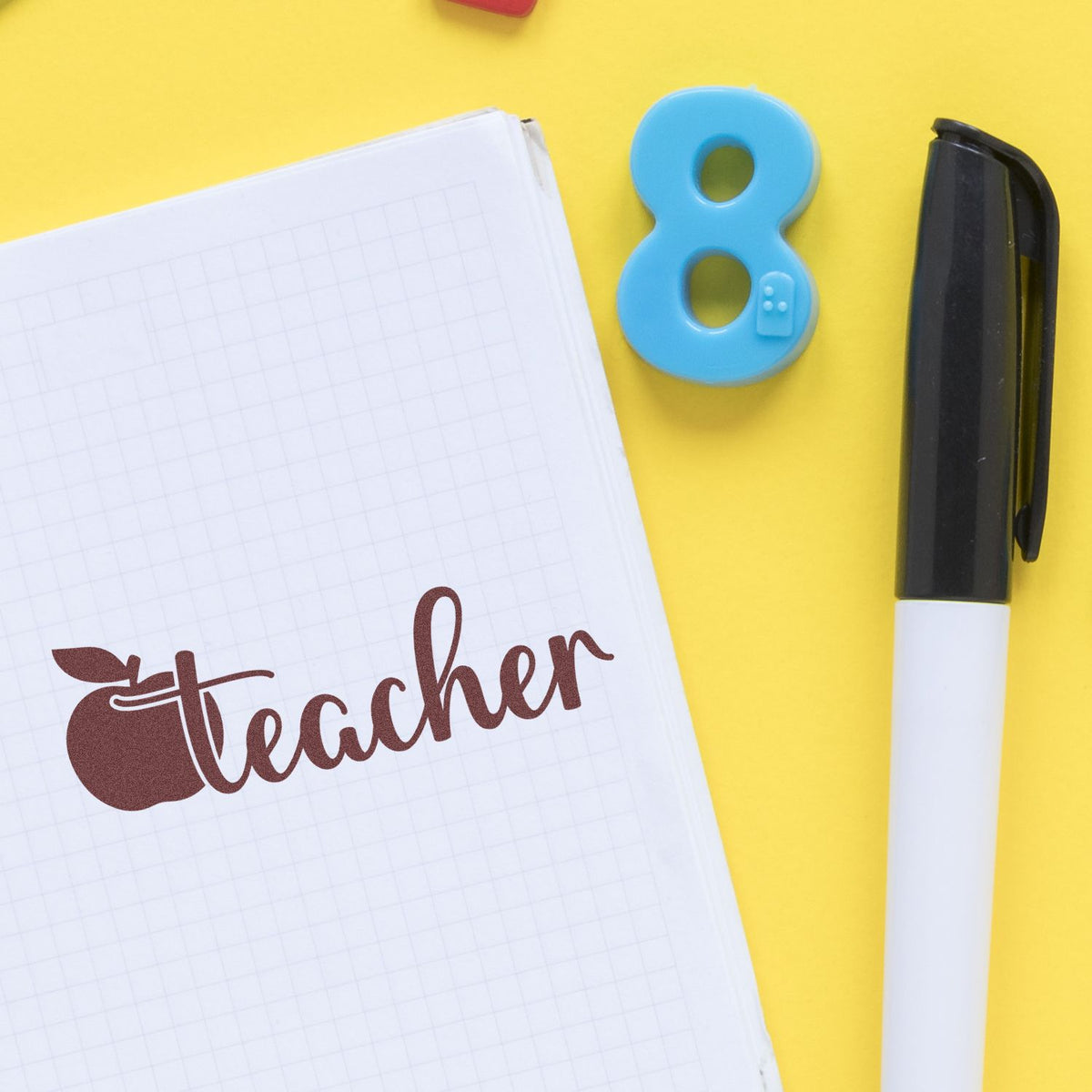 Teacher apple rubber stamp imprint on notebook with marker and number 8, school supply design on yellow background