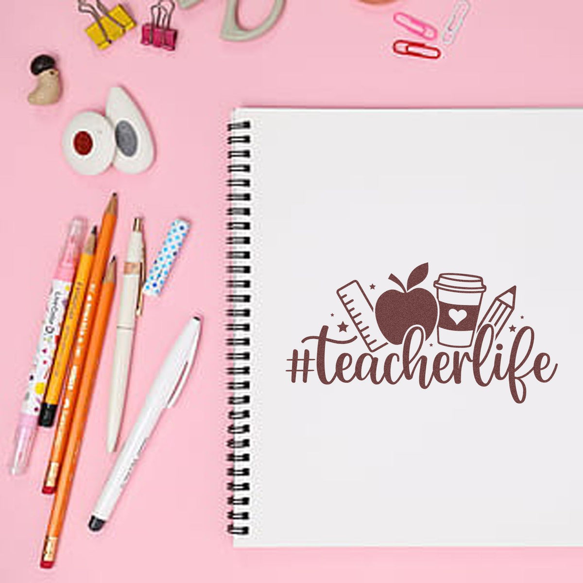 Teacher life rubber stamp design on a spiral notebook with school supplies, ideal for classroom planners and teacher crafts.