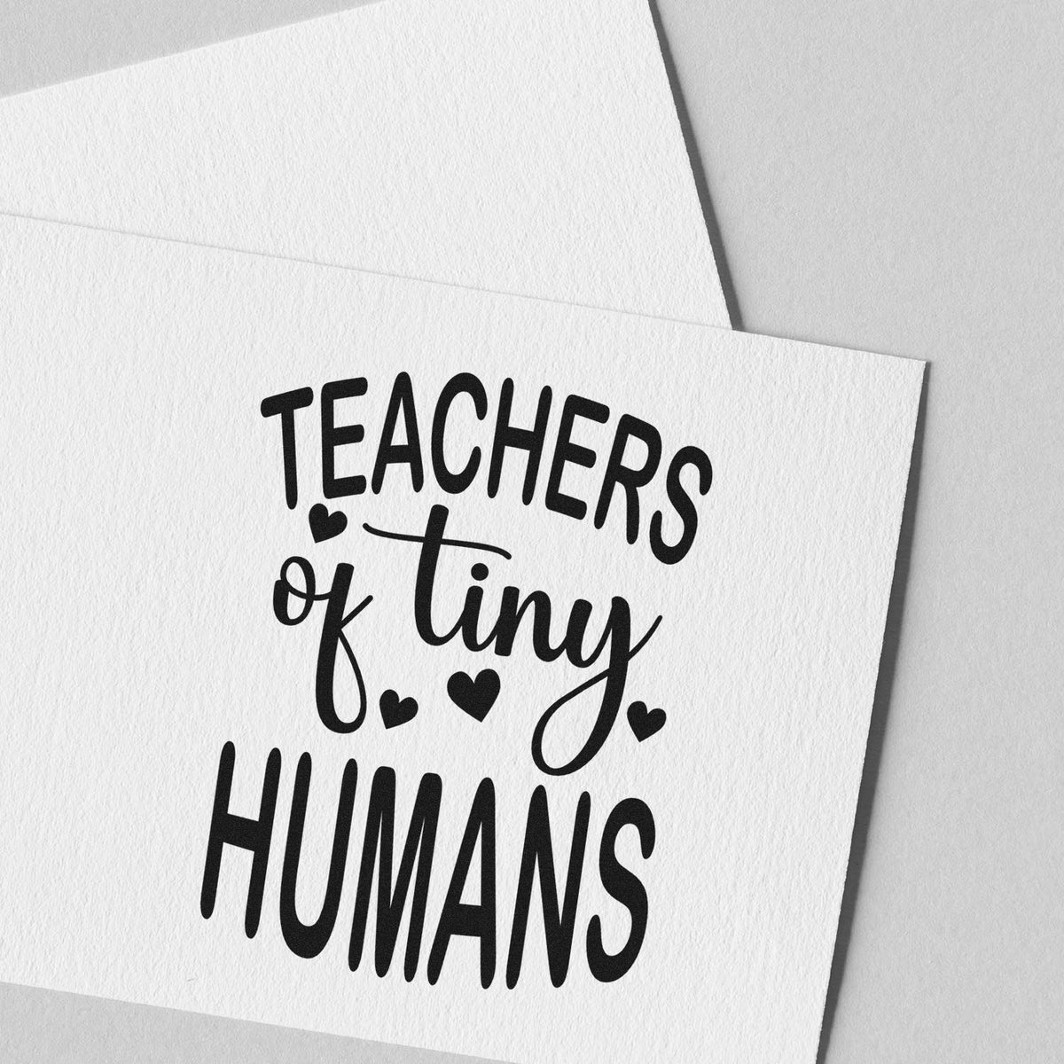 Teachers of tiny humans rubber stamp on white paper, a cute custom teacher appreciation design with hearts.