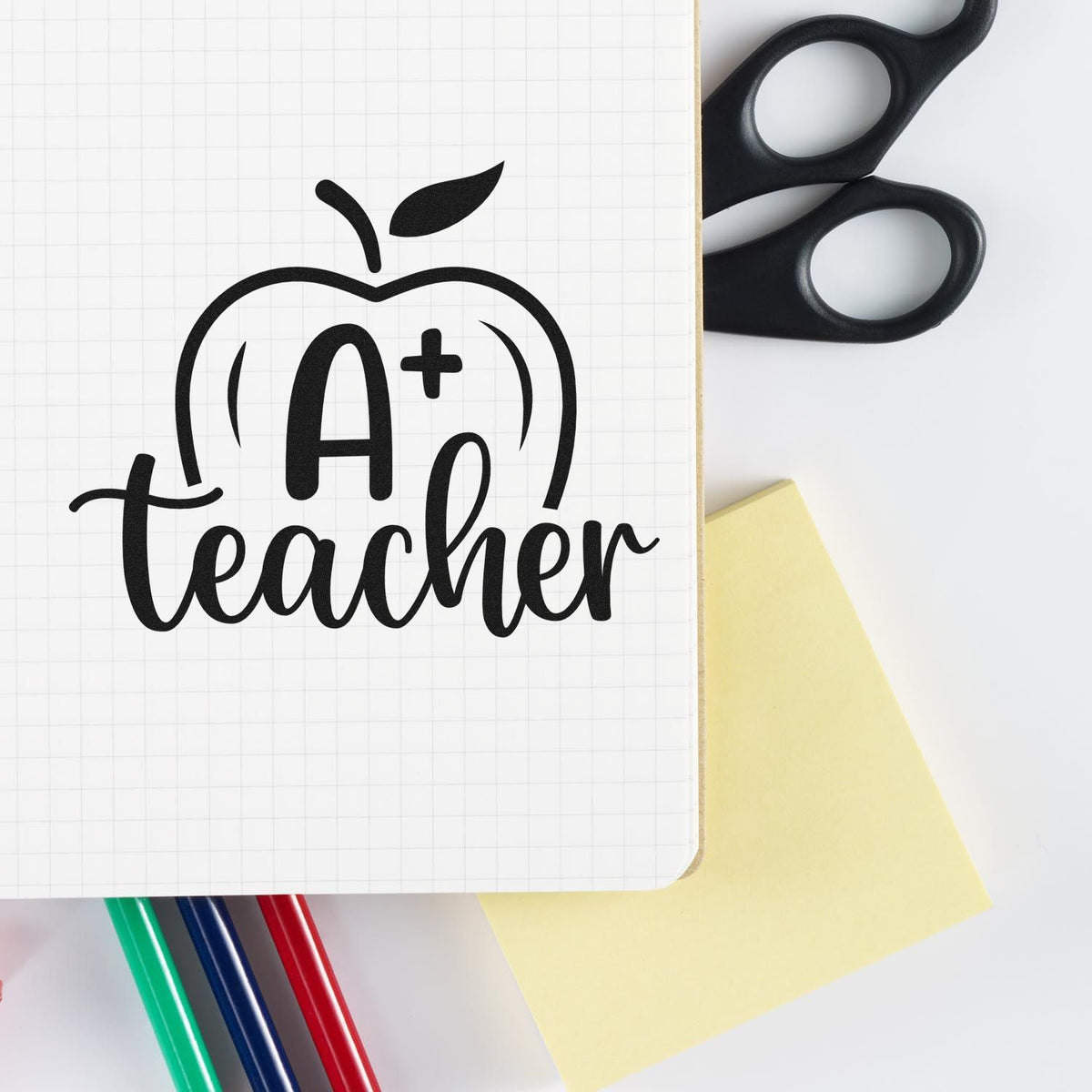 A+ teacher apple rubber stamp design on notebook page with school supplies, perfect for classroom rewards and teacher gifts