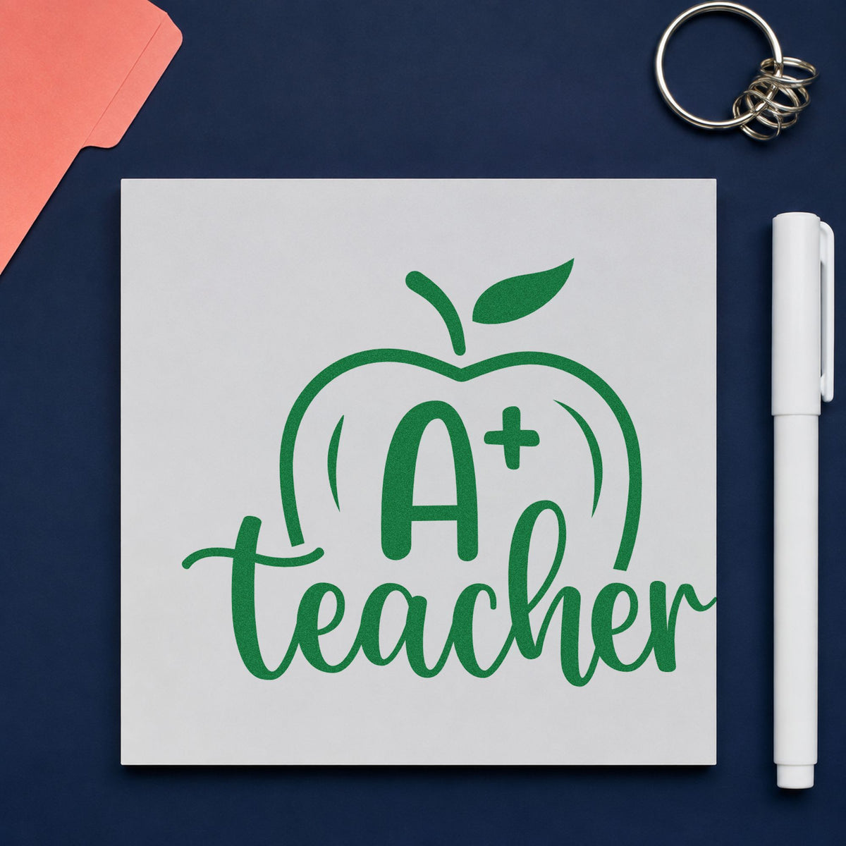 A Plus Teacher Apple craft stamp imprint in green ink on a handmade project, one idea being framed board header.