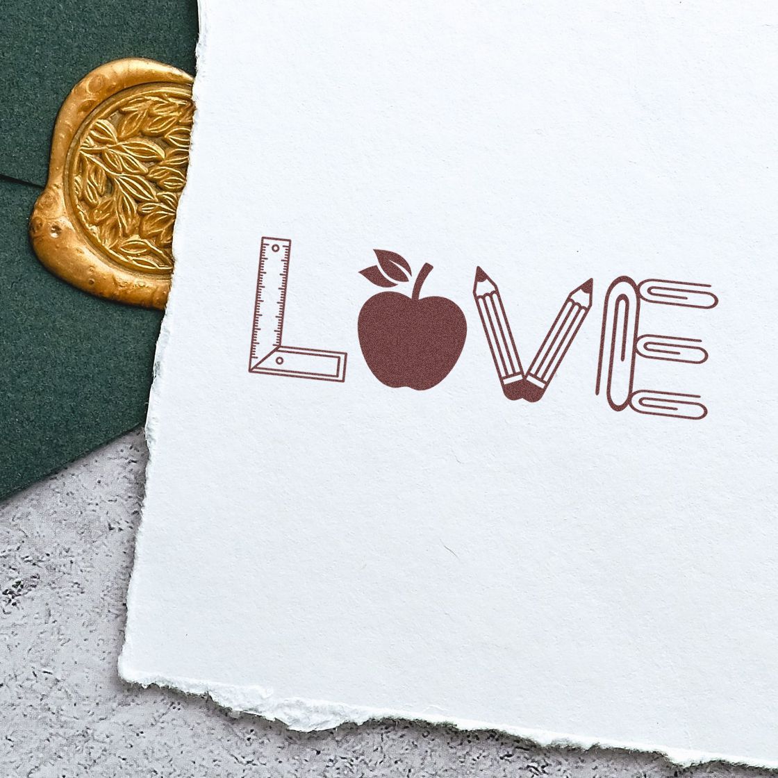Custom rubber stamp design spelling LOVE with school supply icons on paper, ideal for stationery, classroom, or teacher branding.