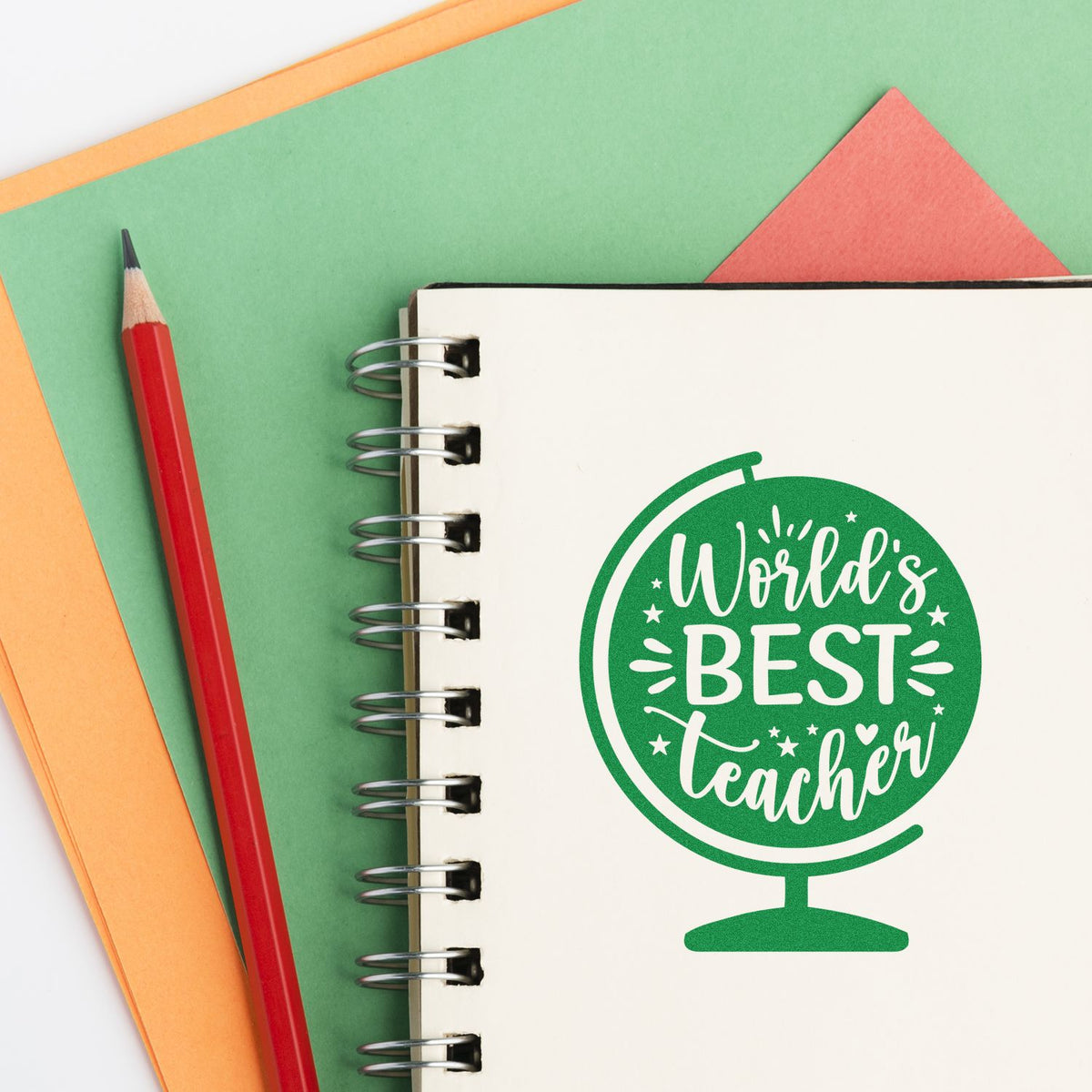 World's Best Teacher rubber stamp design on a notebook, with pencil and colorful paper background for teacher gifts.