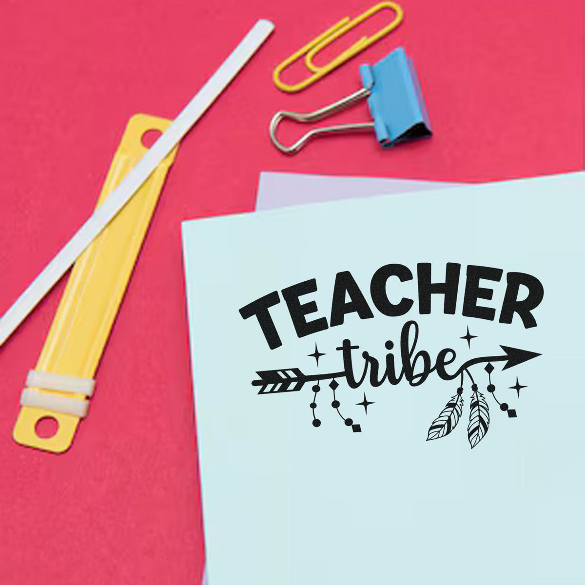 Teacher Tribe rubber stamp design on light blue paper with paper clips and school supplies on a pink background.