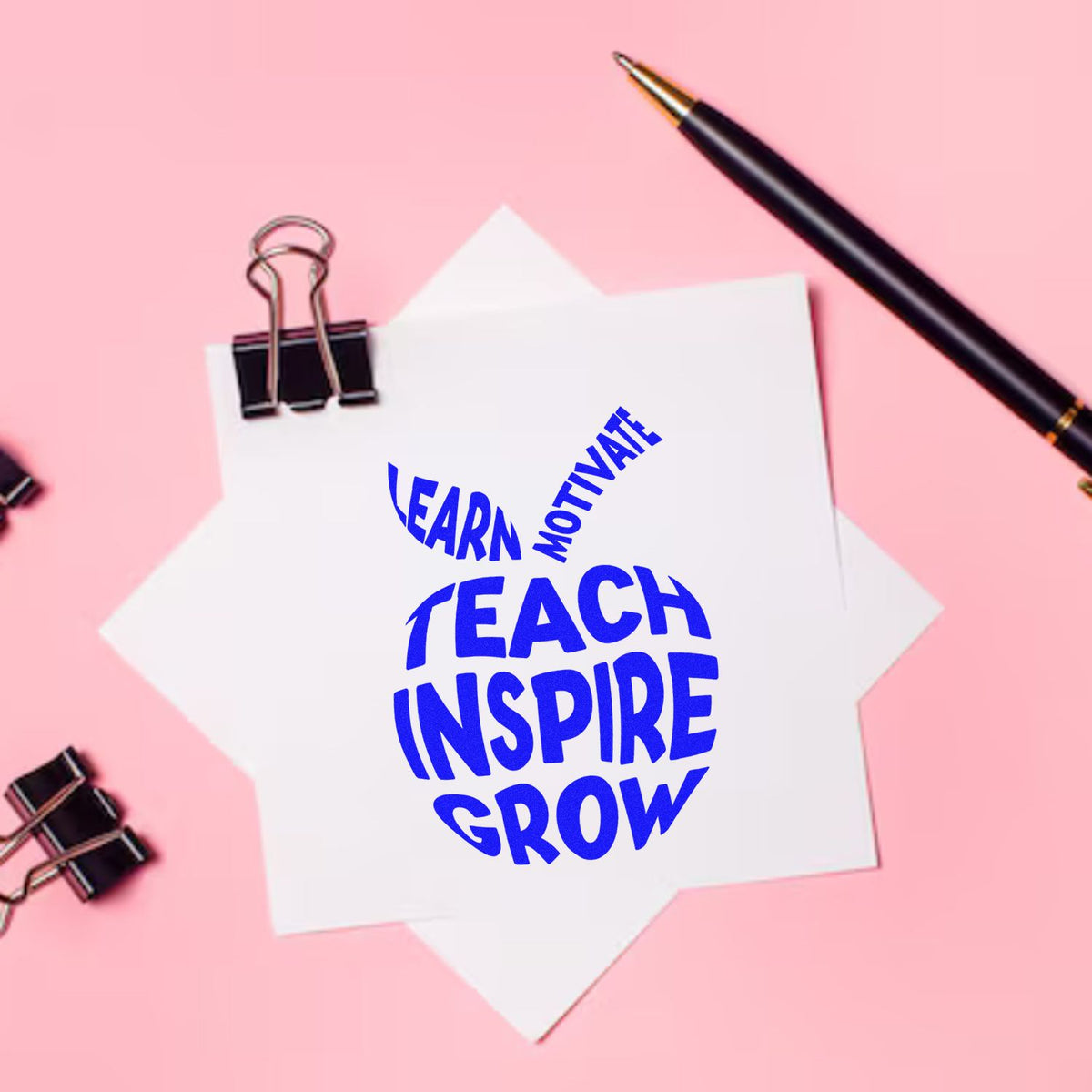 Teacher motivational rubber stamp design reading Learn Motivate Teach Inspire Grow on paper with pen and binder clips.