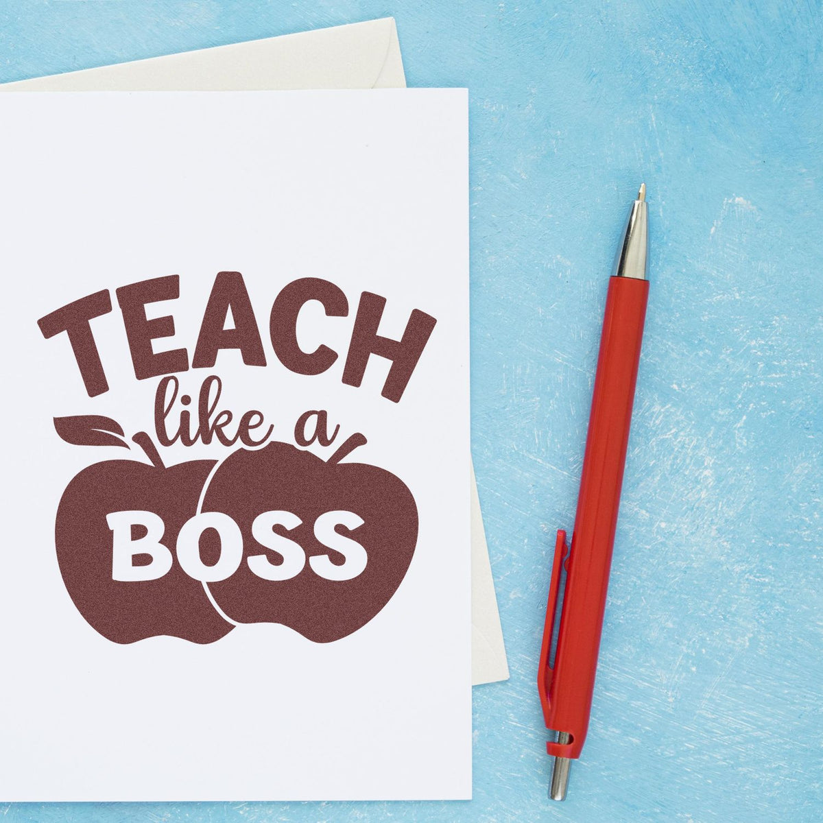 Teacher rubber stamp mockup with Teach like a Boss apple design on paper beside a red pen.