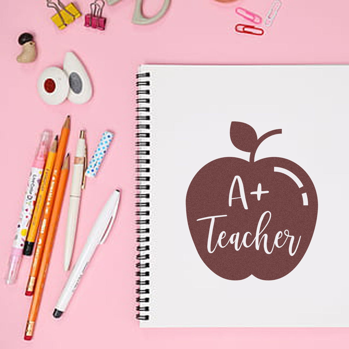 A+ Teacher apple rubber stamp for teachers, shown on a spiral notebook for classroom grading and stationery use.