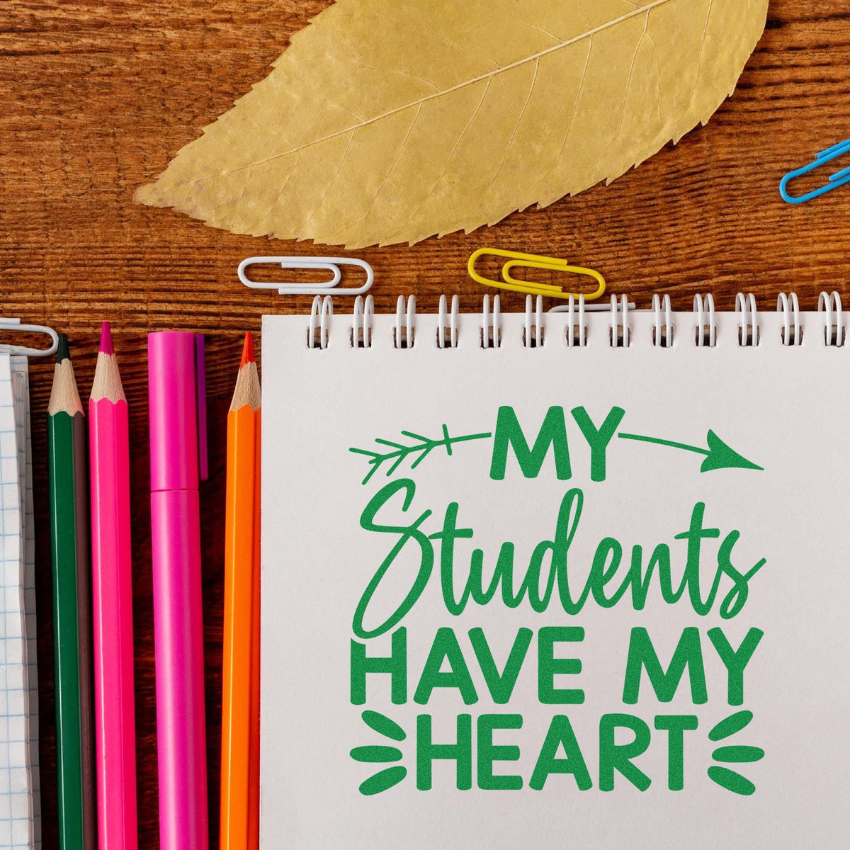 Teacher rubber stamp design reading My Students Have My Heart on a spiral notebook, with pencils and paper clips.