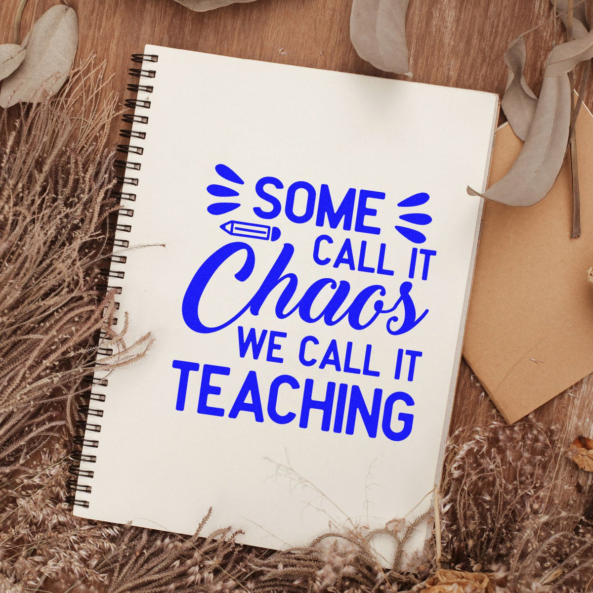 Teacher rubber stamp design on notebook reading Some call it chaos, we call it teaching in bold blue lettering.