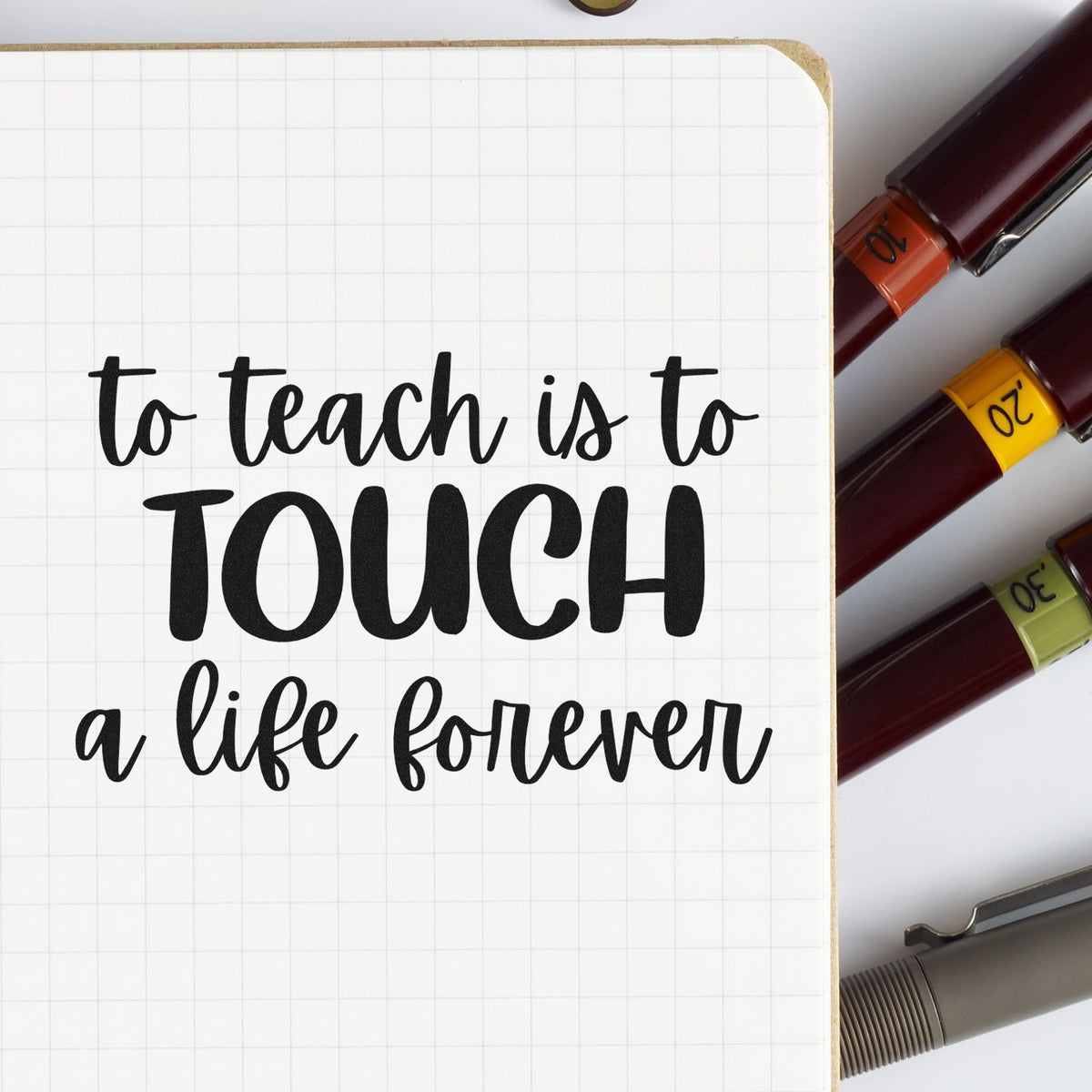 Inspirational teacher rubber stamp quote, To teach is to touch a life forever, on a notebook with markers.