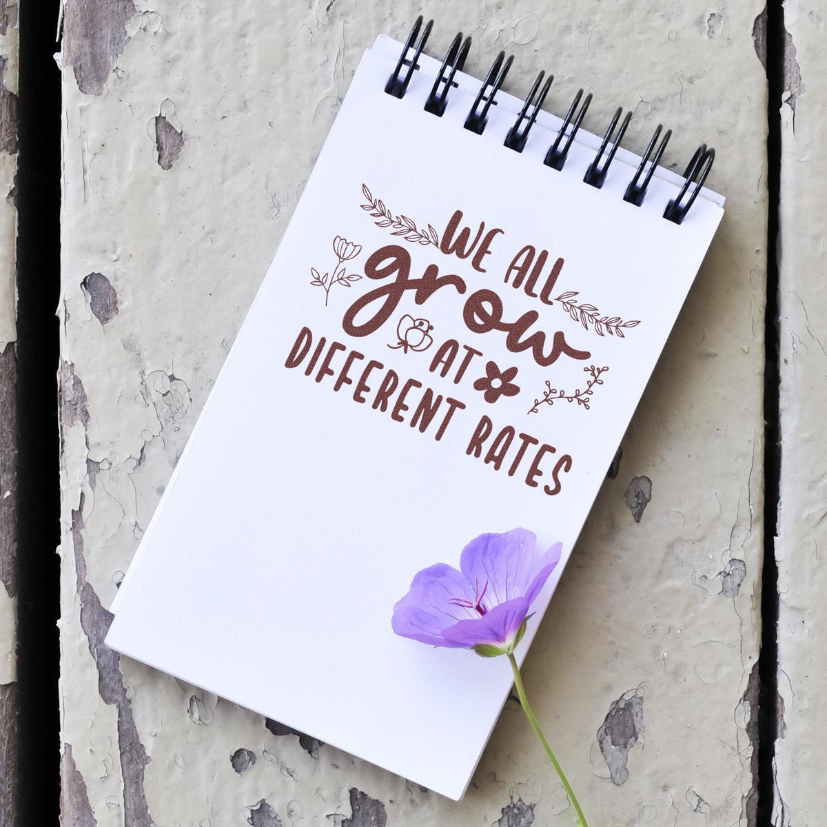 Custom rubber stamp design on notebook reading We all grow at different rates with floral accents.