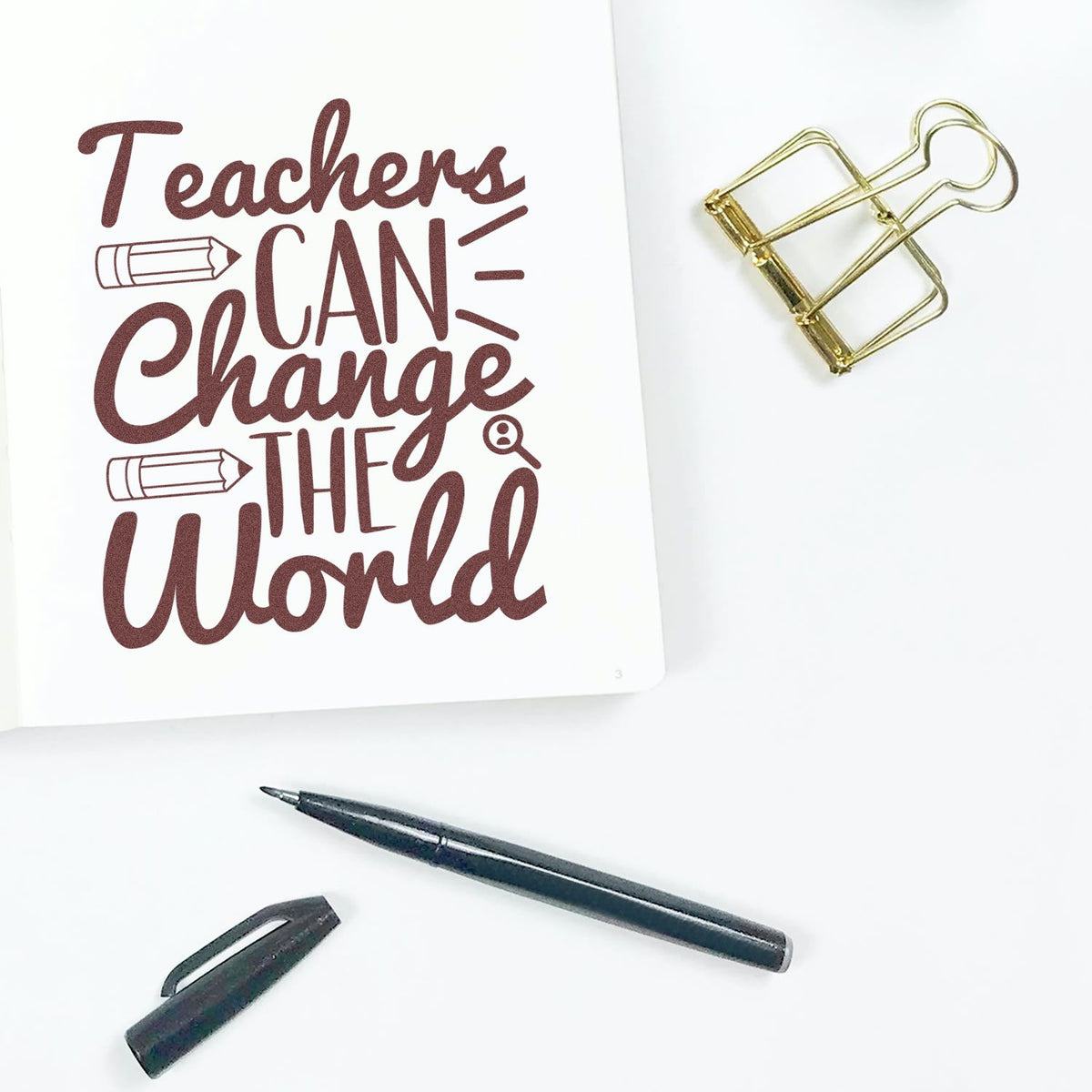 Inspirational teacher rubber stamp design reading Teachers can change the world on white paper with binder clip and pen.