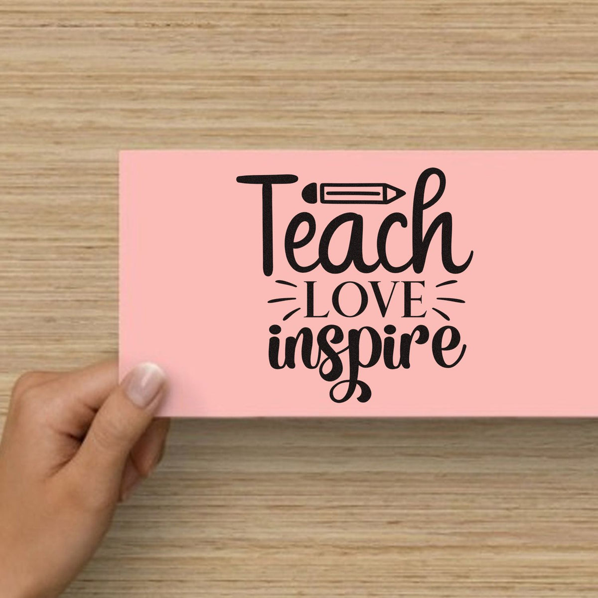 Teach Love Inspire teacher rubber stamp design on pink cardstock, held in hand, with pencil icon for classroom crafting.