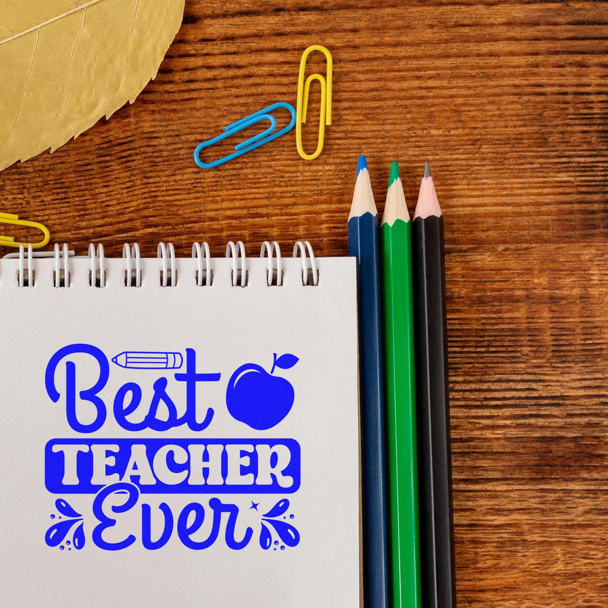 Best Teacher Ever rubber stamp design on notebook with pencils and paper clips, perfect for teacher appreciation gifts.