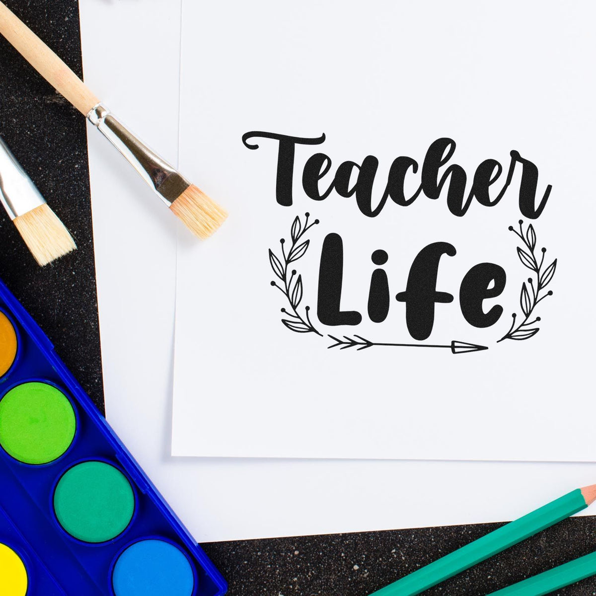 Teacher Life rubber stamp design on paper with paintbrushes and art supplies for classroom craft projects.