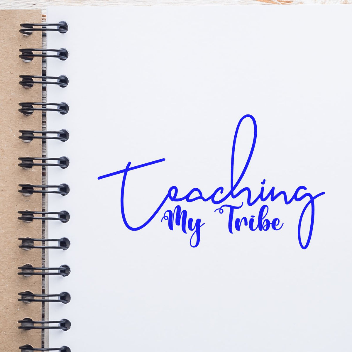 Blue Teaching My Tribe rubber stamp on a spiral notebook page, ideal for teacher crafts and journaling.