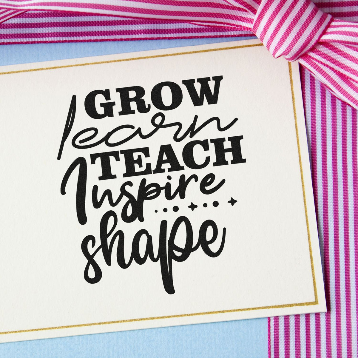 Inspirational rubber stamp design with Grow Learn Teach Inspire Shape lettering on a white card with pink striped ribbon.