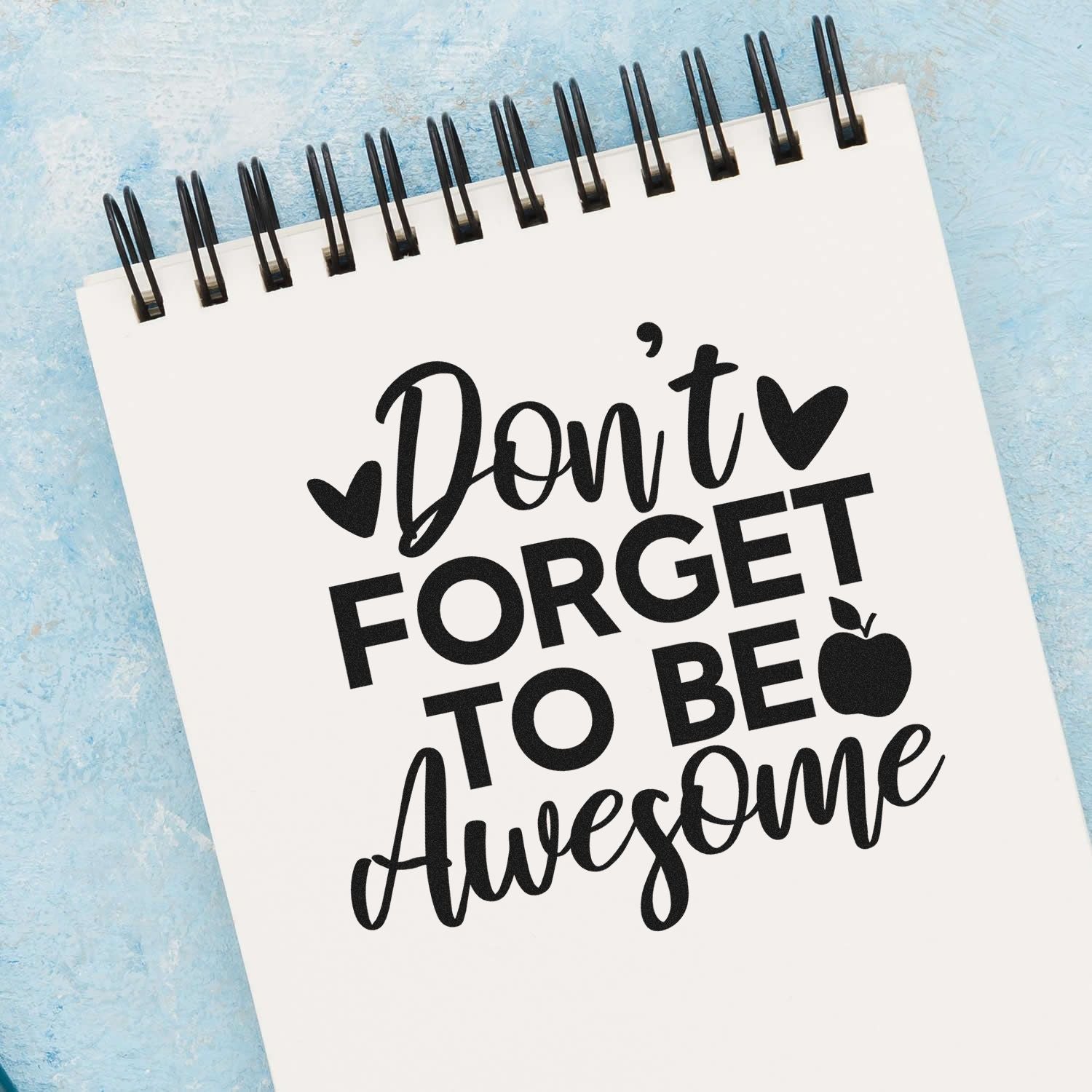 Motivational rubber stamp design reading Don't Forget to Be Awesome on a spiral notebook with hearts and apple icon.
