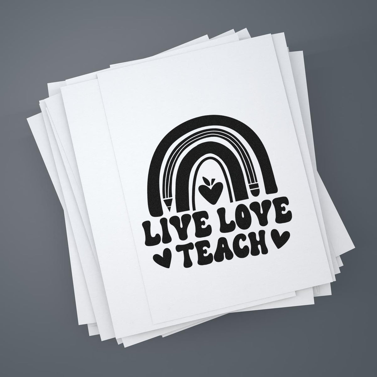 Live Love Teach rubber stamp design with rainbow and heart on stacked white paper sheets for teacher crafts and stationery.